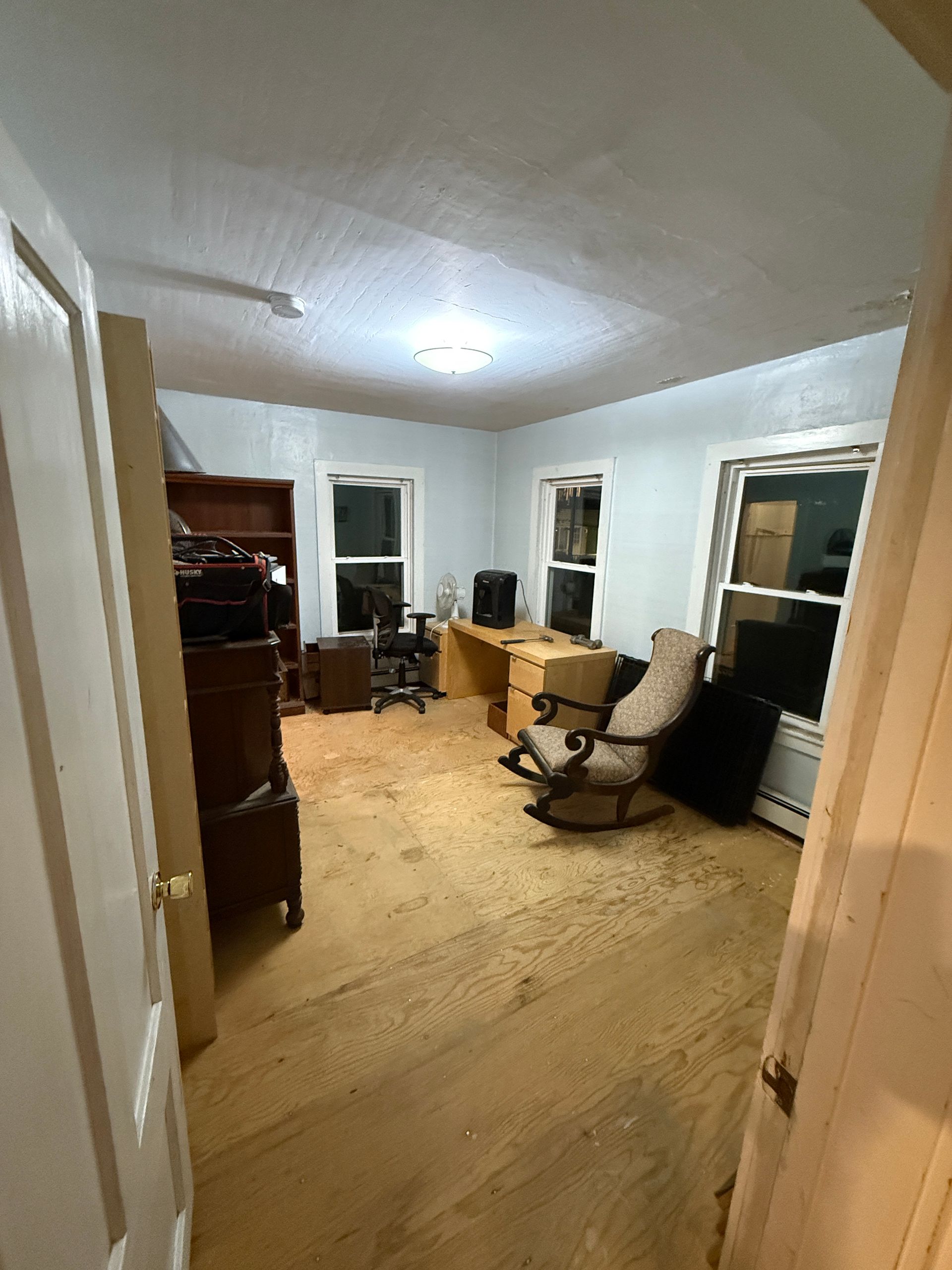 Room interior with light blue walls, wooden floors, furniture, and two windows.