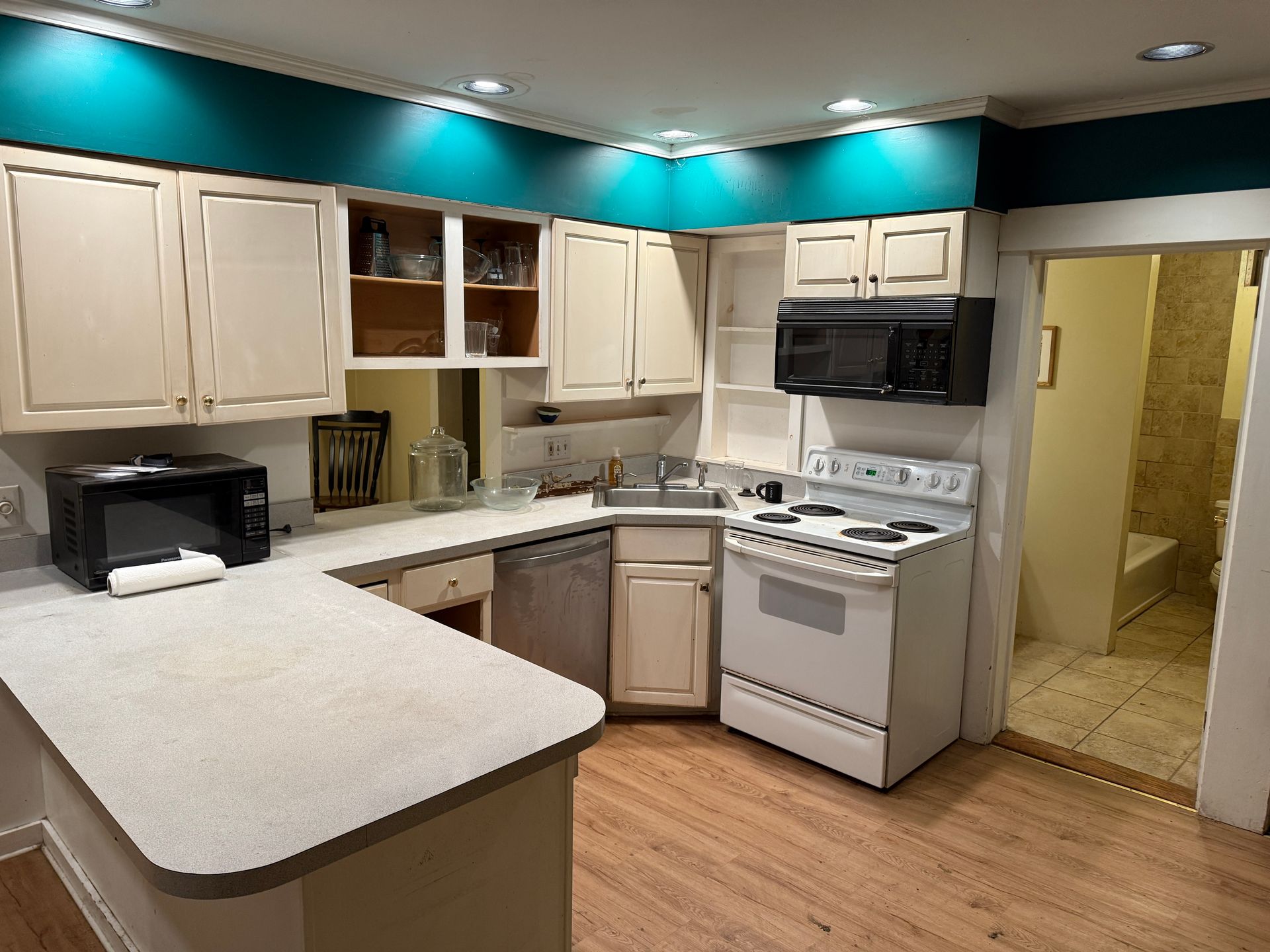 Kitchen with white cabinets, appliances, and turquoise trim. A small doorway leads to a bathroom.