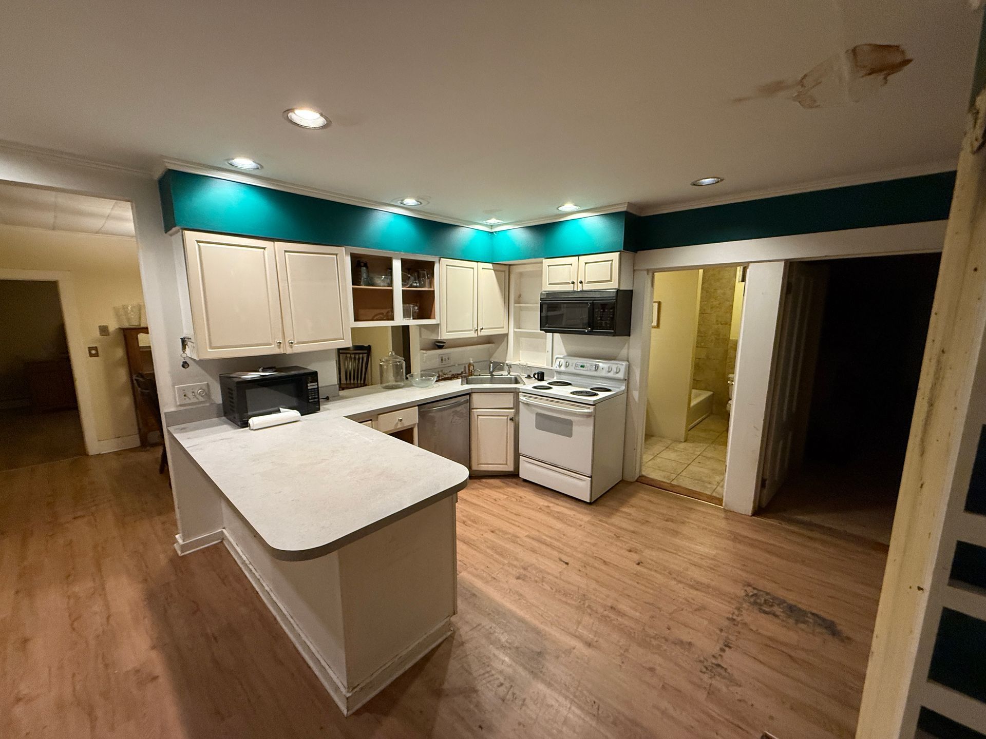 Kitchen with white cabinets, turquoise accents, and light wood floors. Includes a microwave and stove.