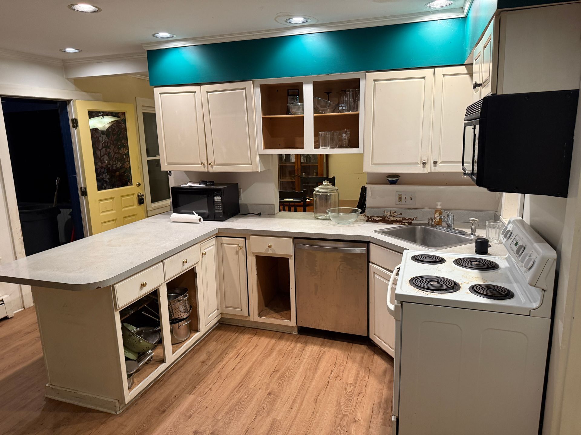 Kitchen with off-white cabinets, turquoise wall, island, stove, and microwave.