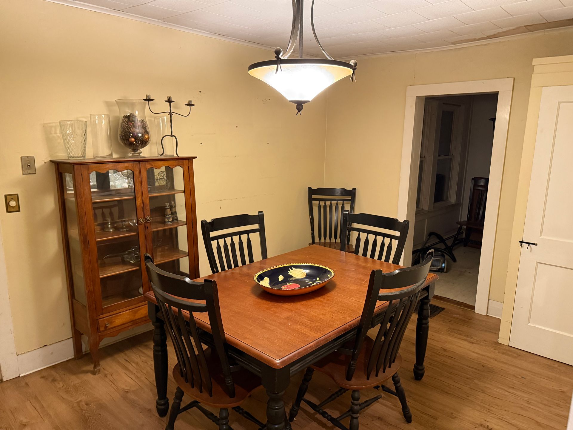 Dining room with wooden table, black chairs, glass cabinet, and light fixture.