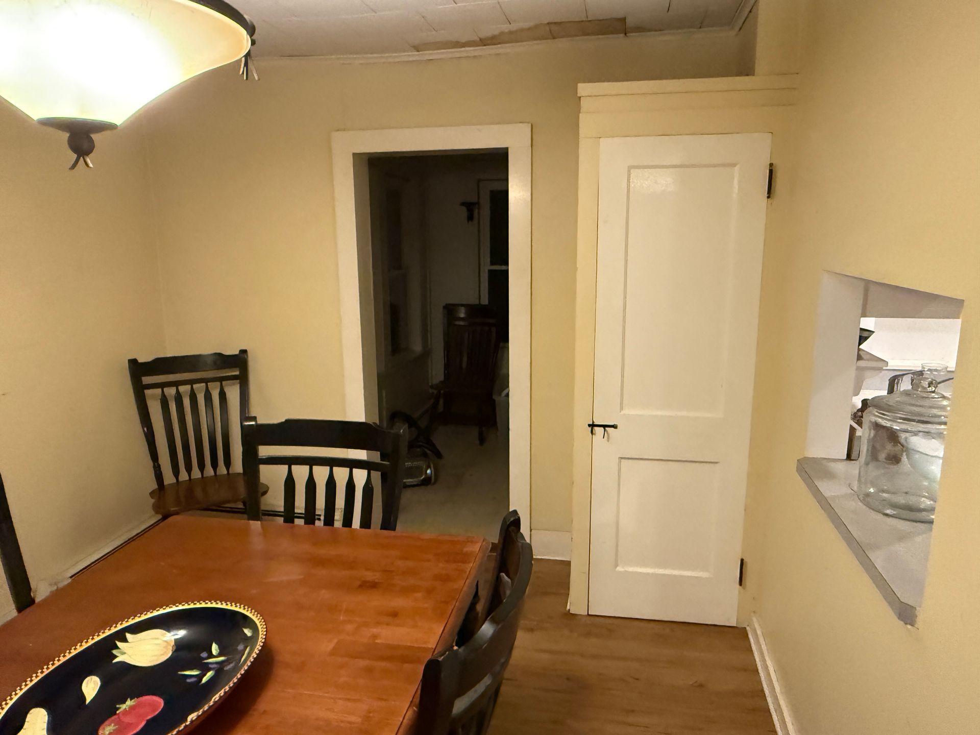 Dining room with table, chairs, door, and a small window. Light yellow walls and wood floor.