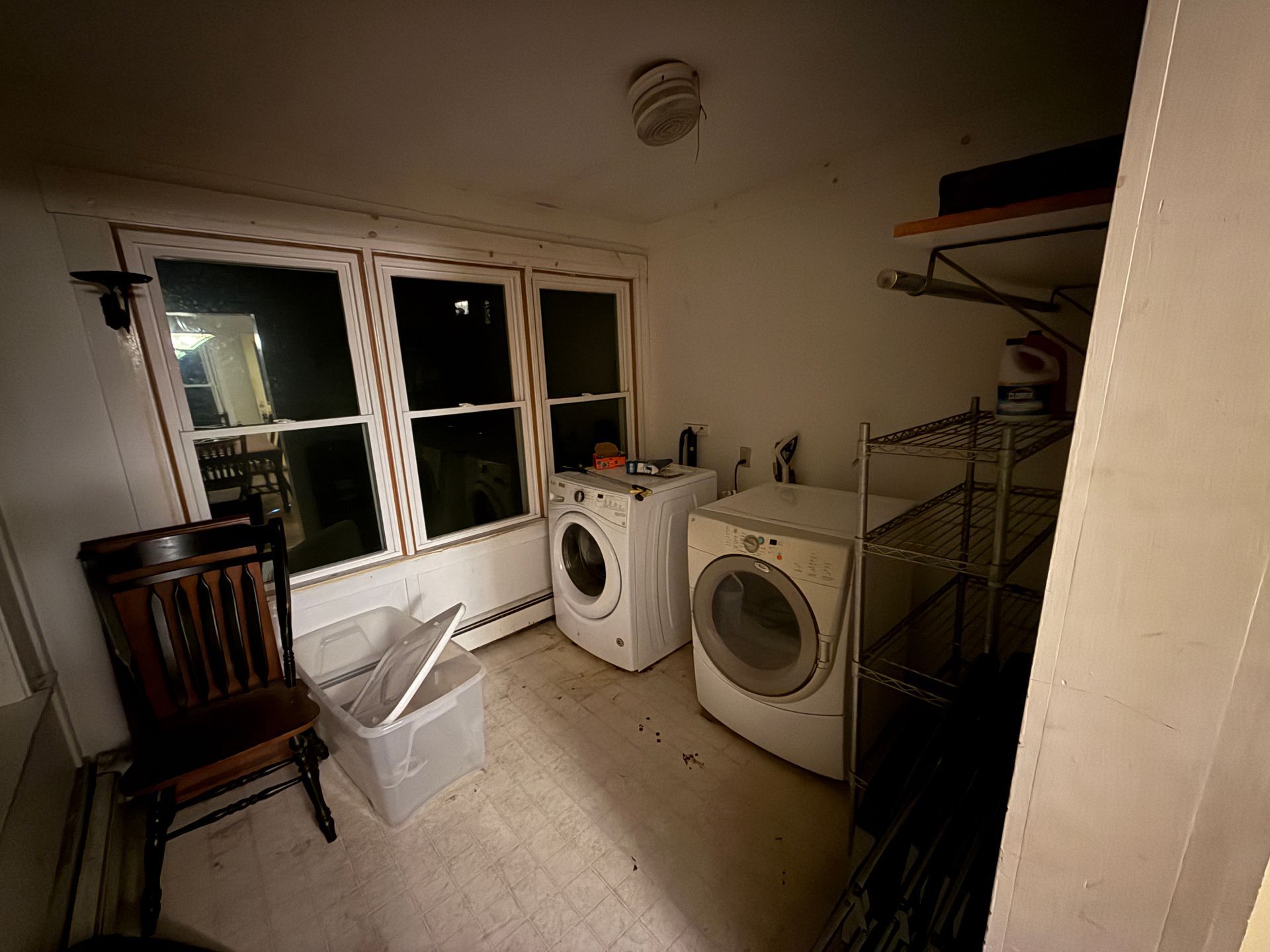 Laundry room with washer, dryer, windows, shelving, chair, and storage container.