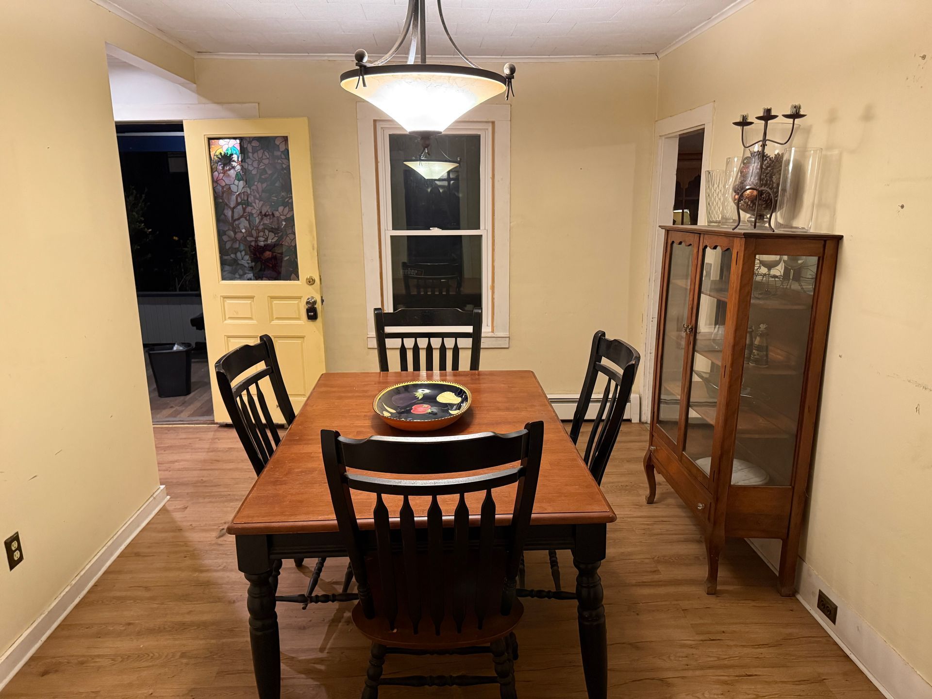 Dining room with wooden table, black chairs, and a glass-front cabinet. Yellow walls and door.