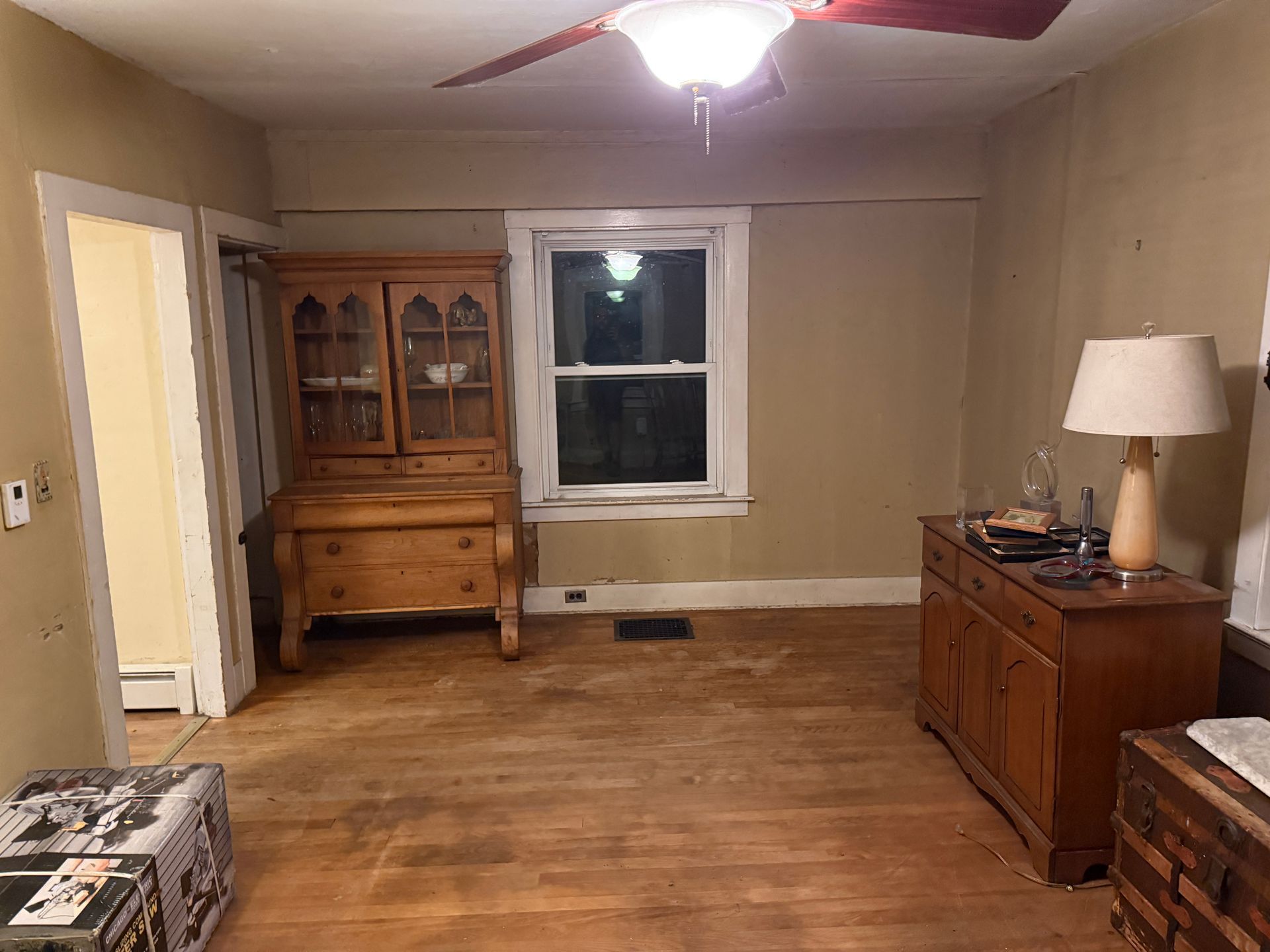 A room with wooden furniture and floors, window, doorway, and ceiling fan. Walls are painted a light tan.