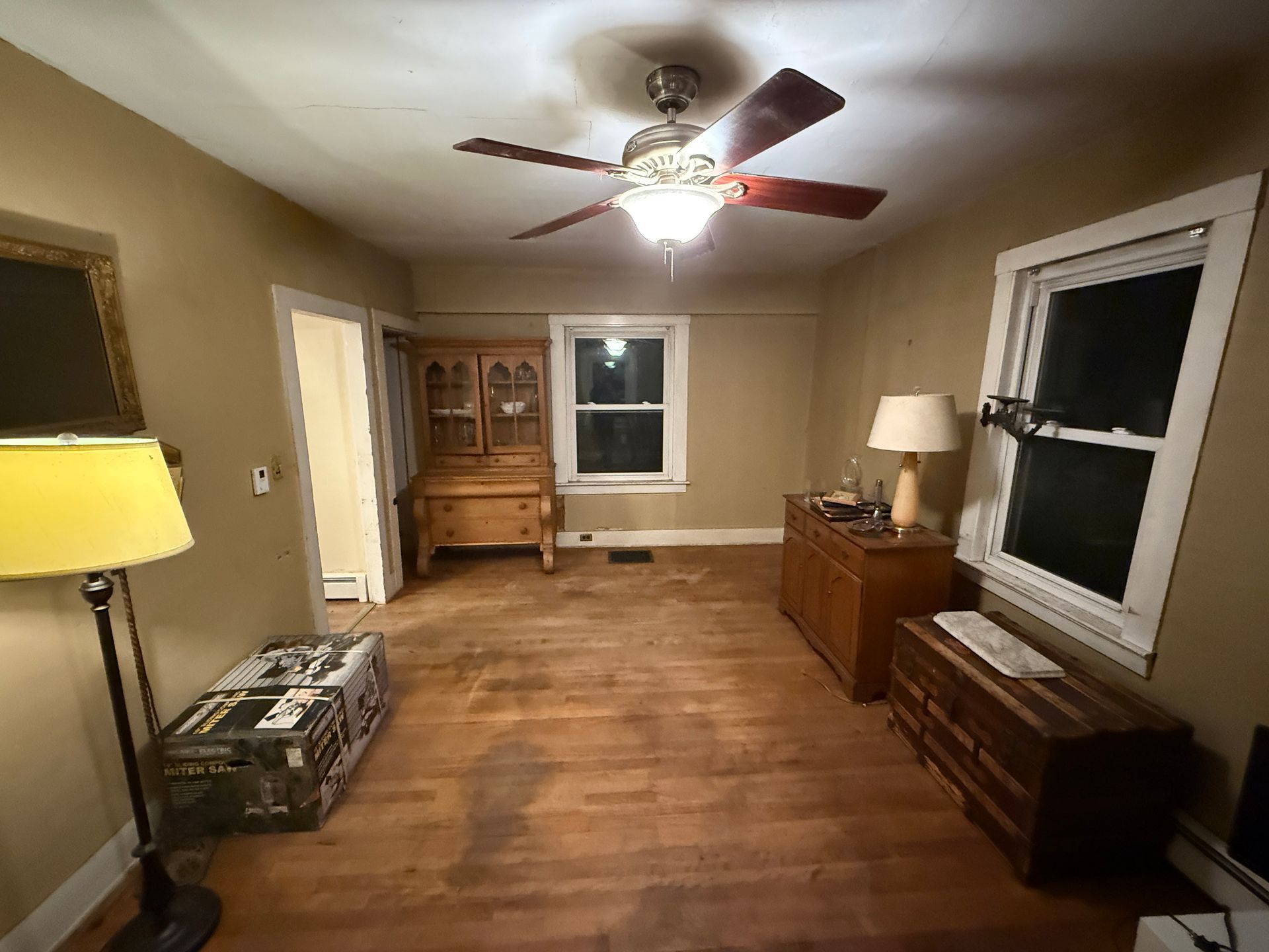 Room with wood floor and furniture: hutch, chest, dresser, lamp, ceiling fan. Window and door visible.