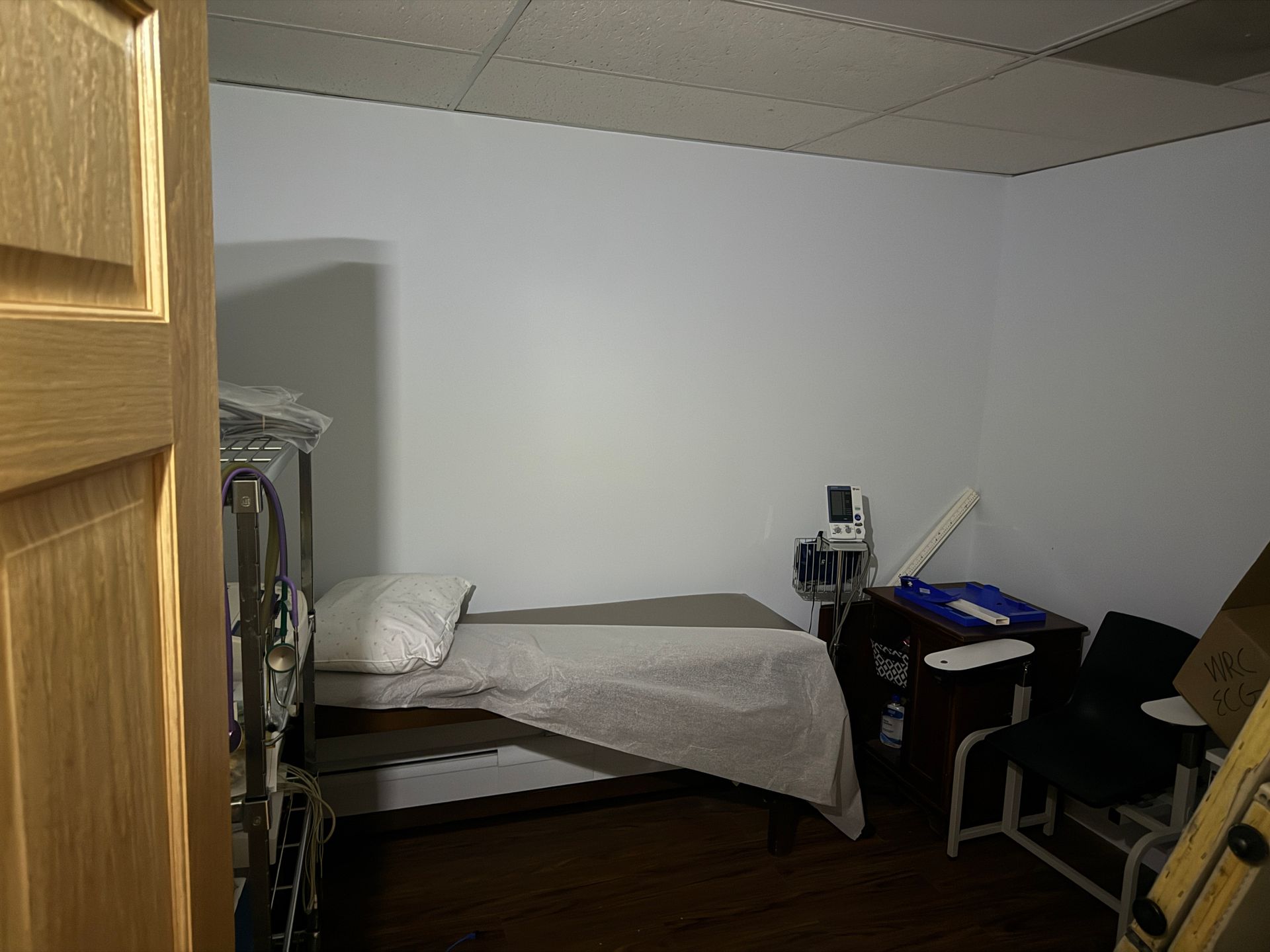 Medical examination room with a bed, equipment, and a wooden door.