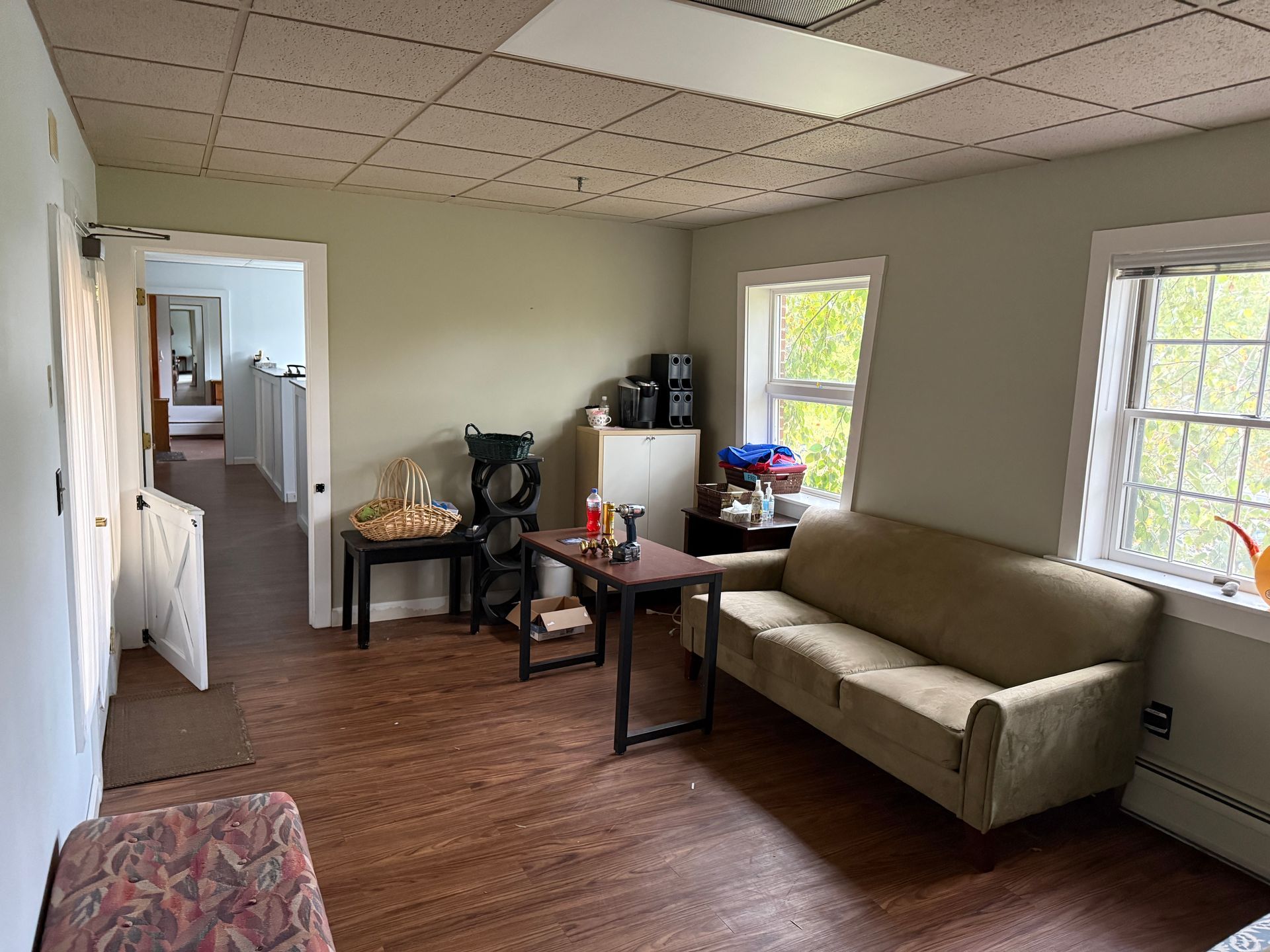 Room with couch, tables, and windows. Another room visible through open doorway.