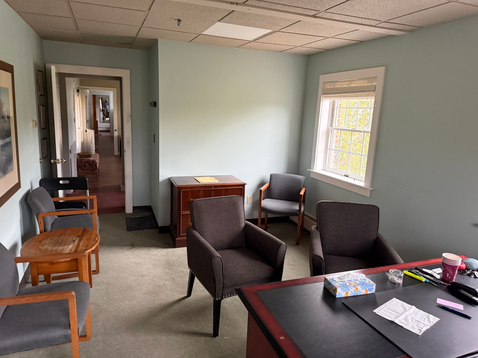 Office with chairs, desk, and a window. Light blue walls and a doorway leading to a hallway.