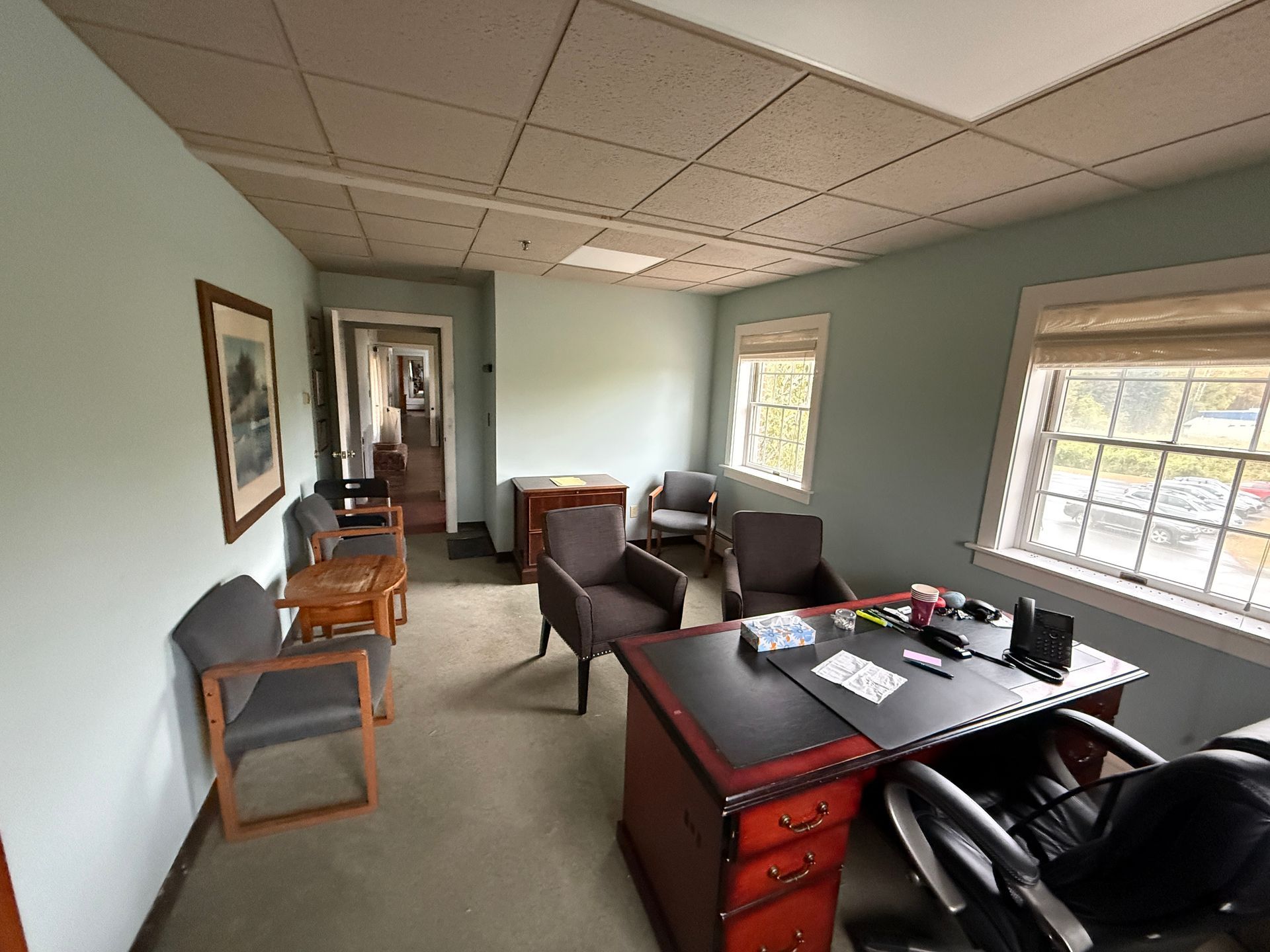 Office with desk, chairs, windows, and framed artwork on the wall. Pale green walls and a dropped ceiling.