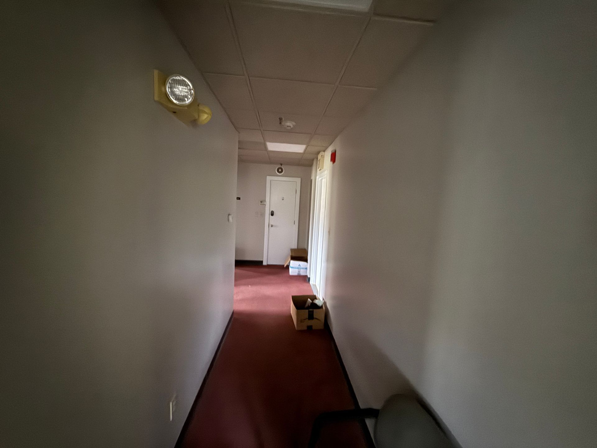 Narrow hallway with red carpet and white walls. A door is at the end of the hall.