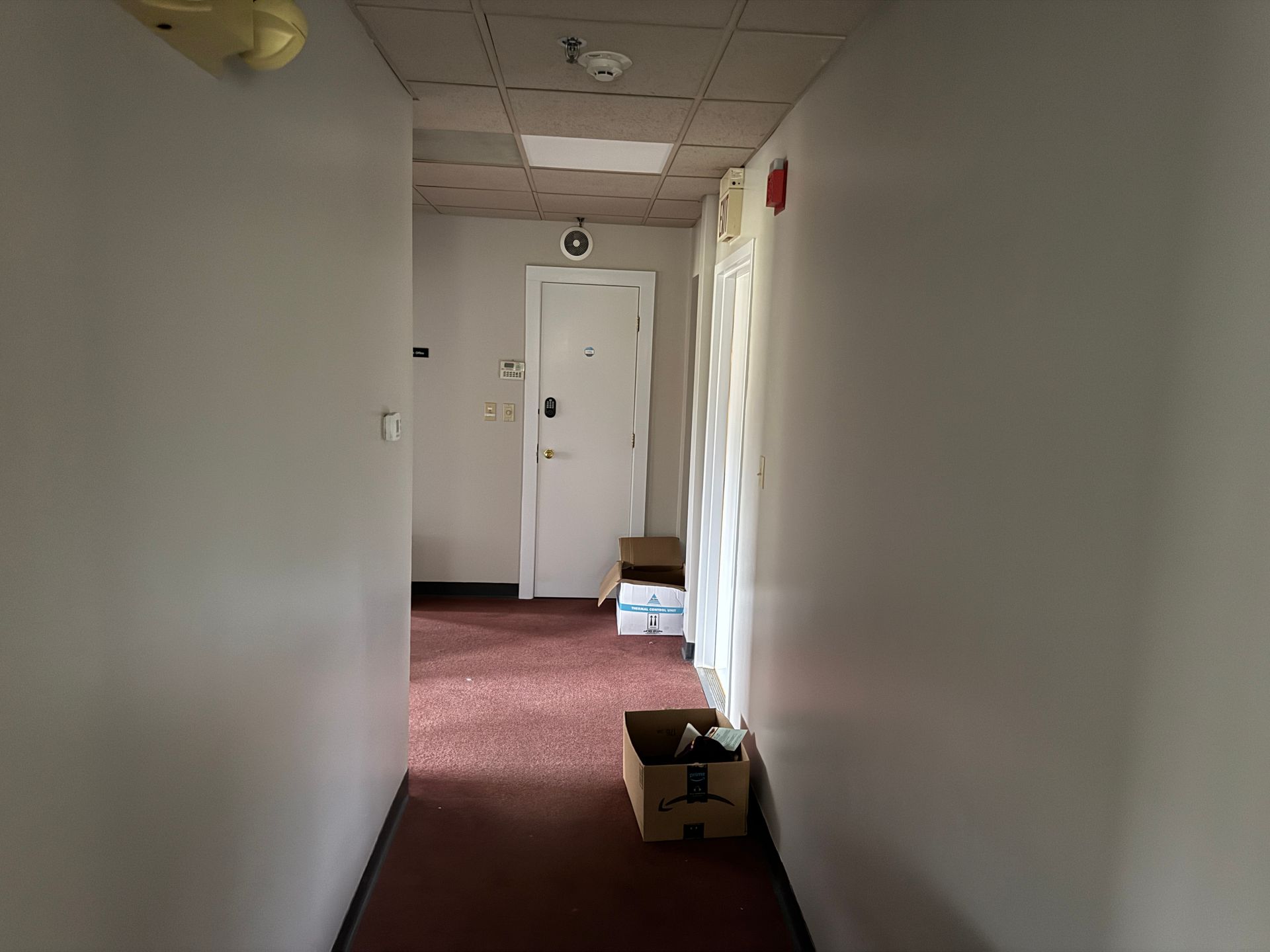 Hallway with white walls, red floor, and a closed door at the end.