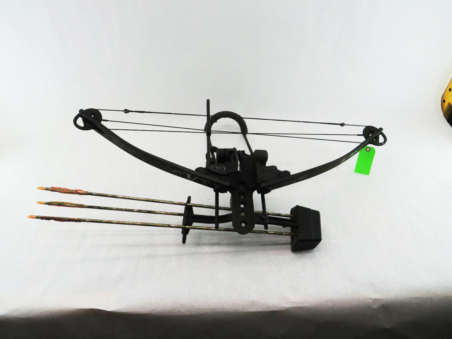 Black crossbow with arrows, set on a white surface. Green tag attached.