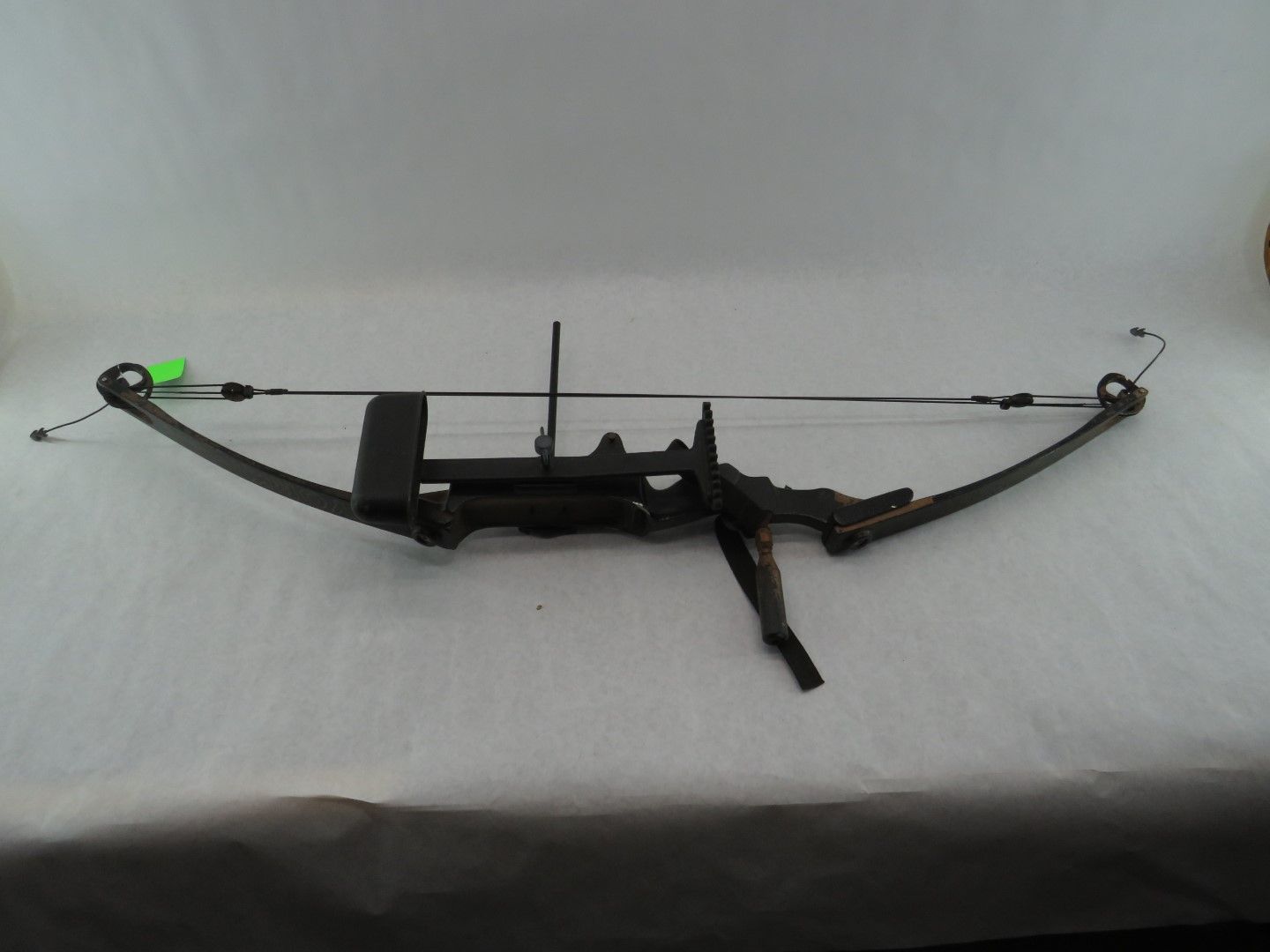 Compound bow on a white surface, dark metallic color, with a bow string and attached accessories.