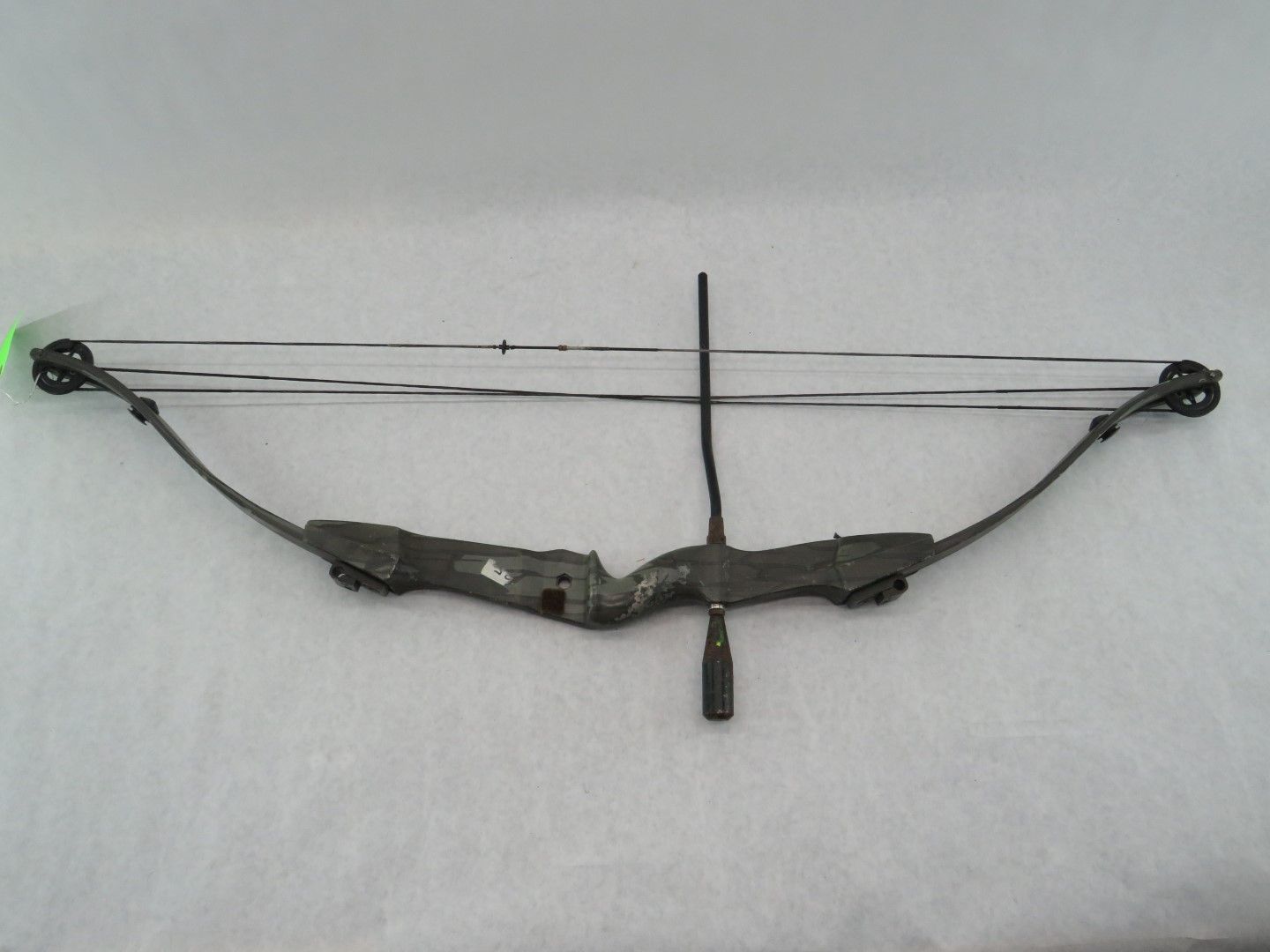 Compound bow with dark limbs and a center stabilizer on a neutral background.