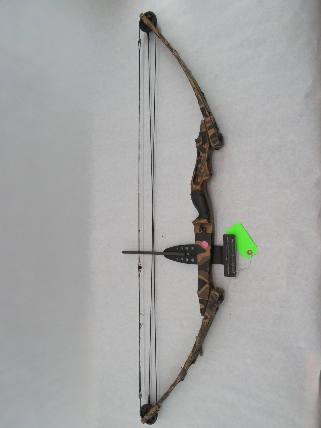 Camouflage compound bow with black and gray strings, and a sight attachment.