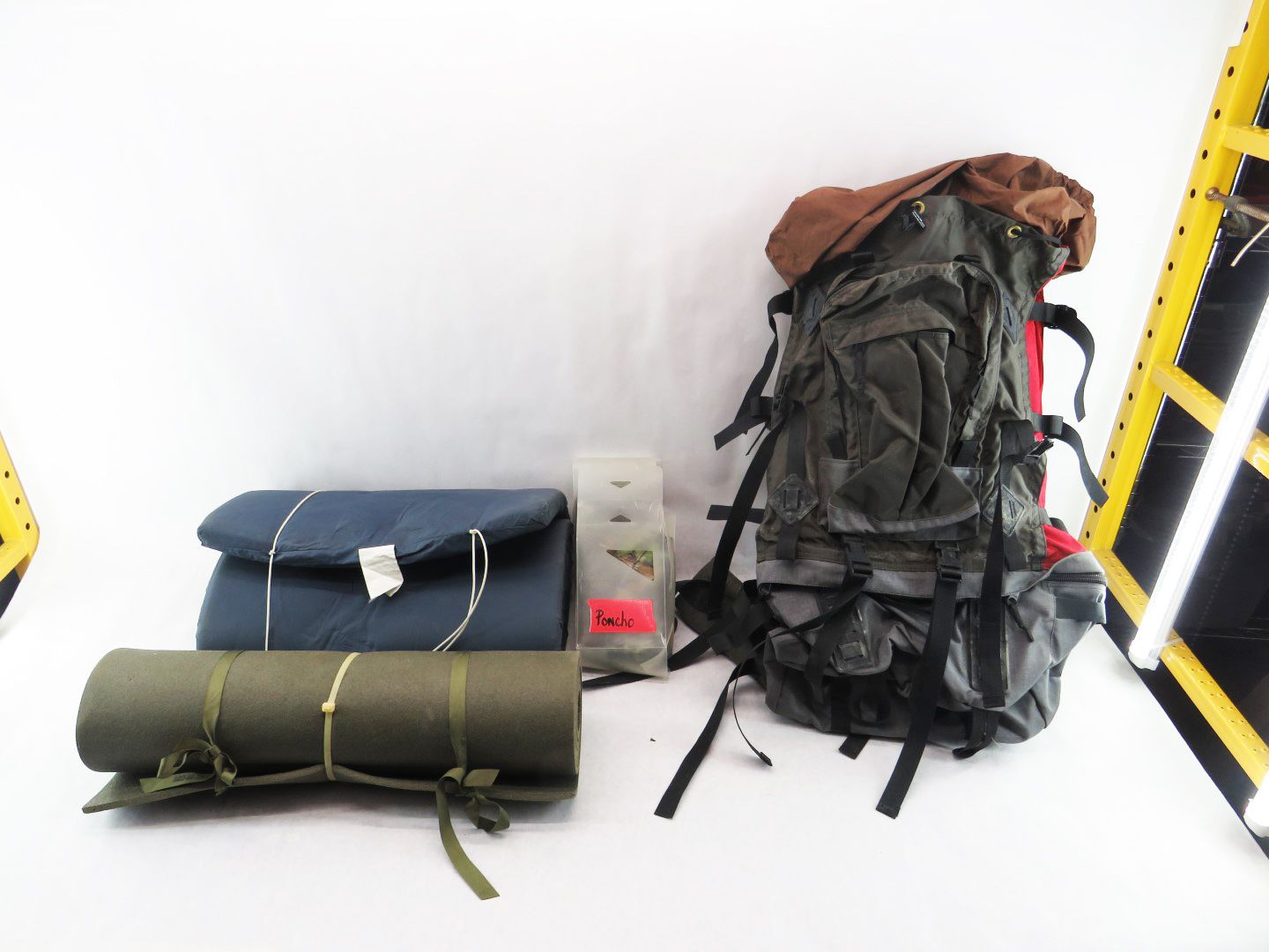 Camping gear: backpack, sleeping bag, rolled mat, and container on a white background.