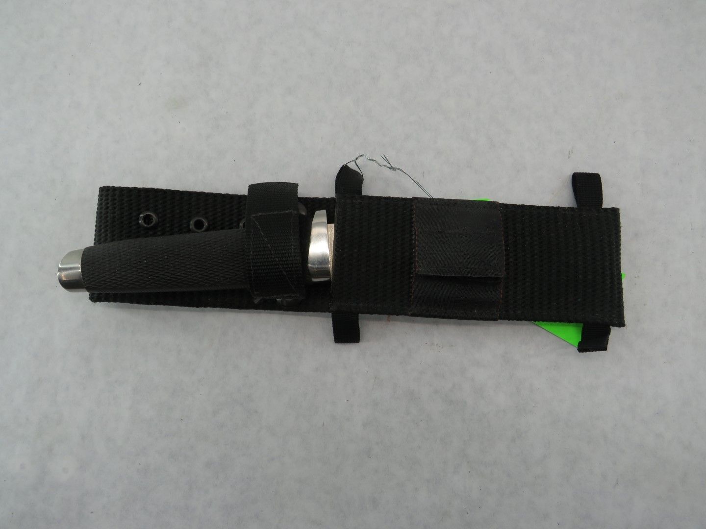 Black nylon sheath holding a silver-tipped flashlight; green tab visible; on a white background.