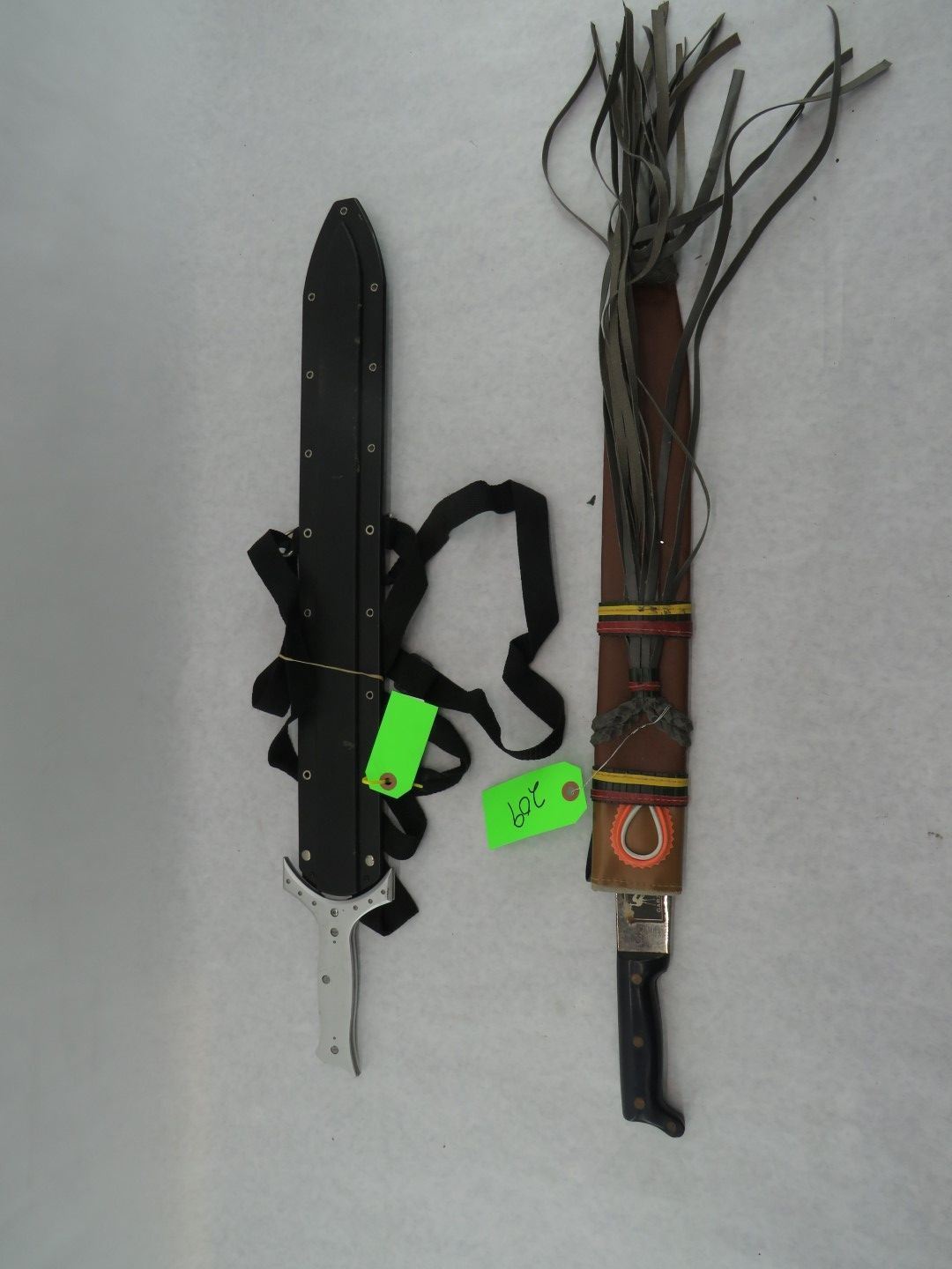 Two sheathed knives with handles; one black with shoulder strap, one leather with fringe.
