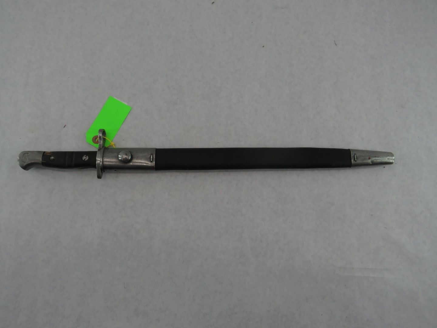 Bayonet with black handle and sheath, and a green price tag.