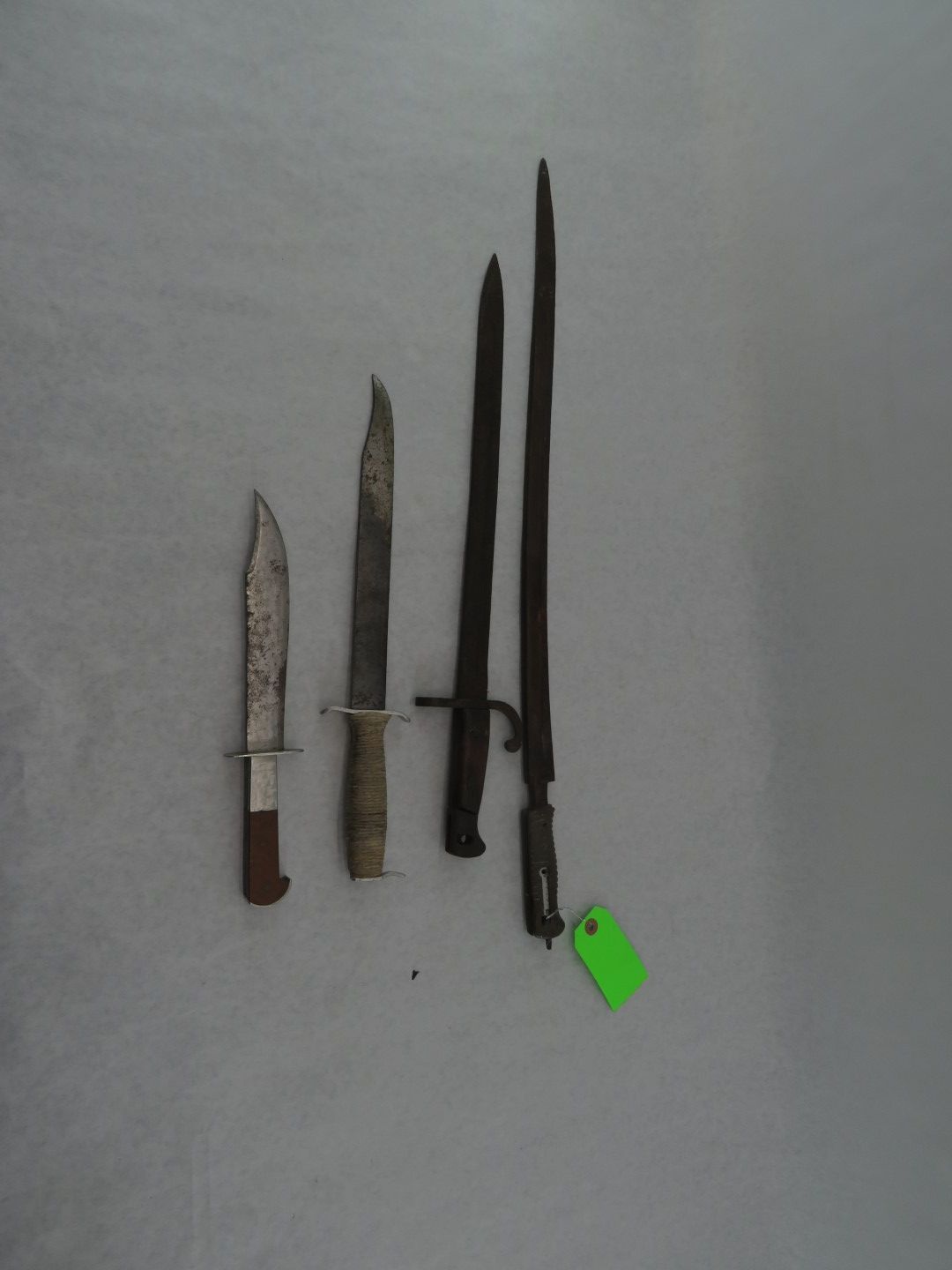 Four antique knives and bayonets displayed on a white surface.