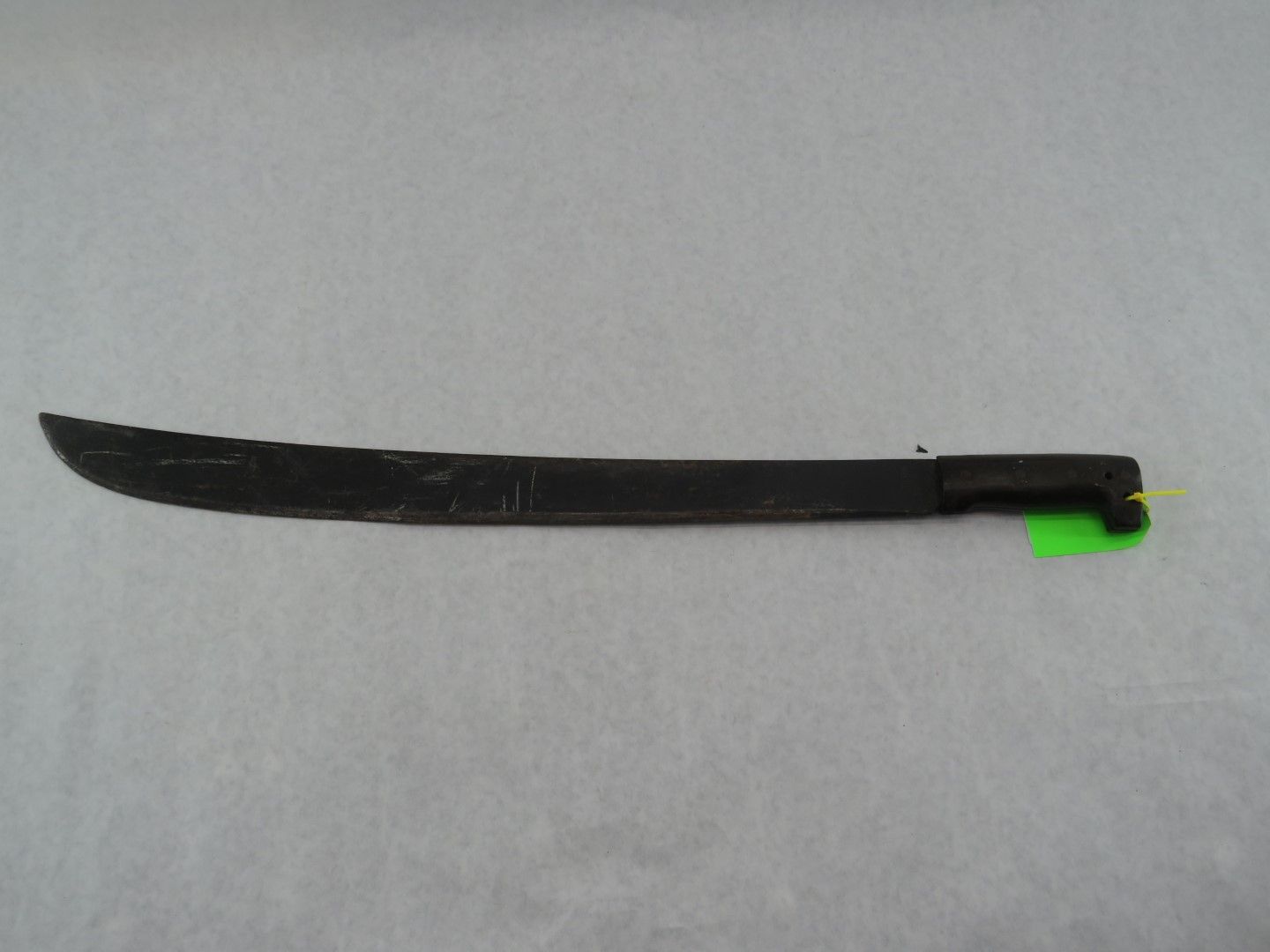 Dark machete on a white surface, handle on right, curved blade extending left.