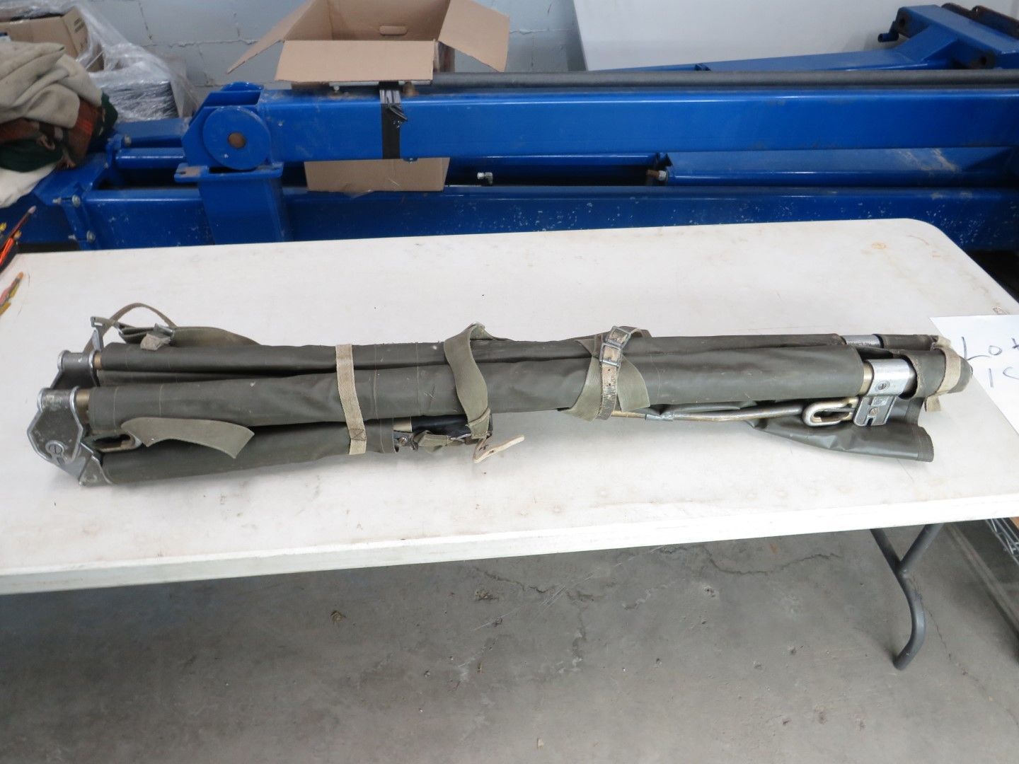 Folded green canvas tripod on a white table. Straps secure it.