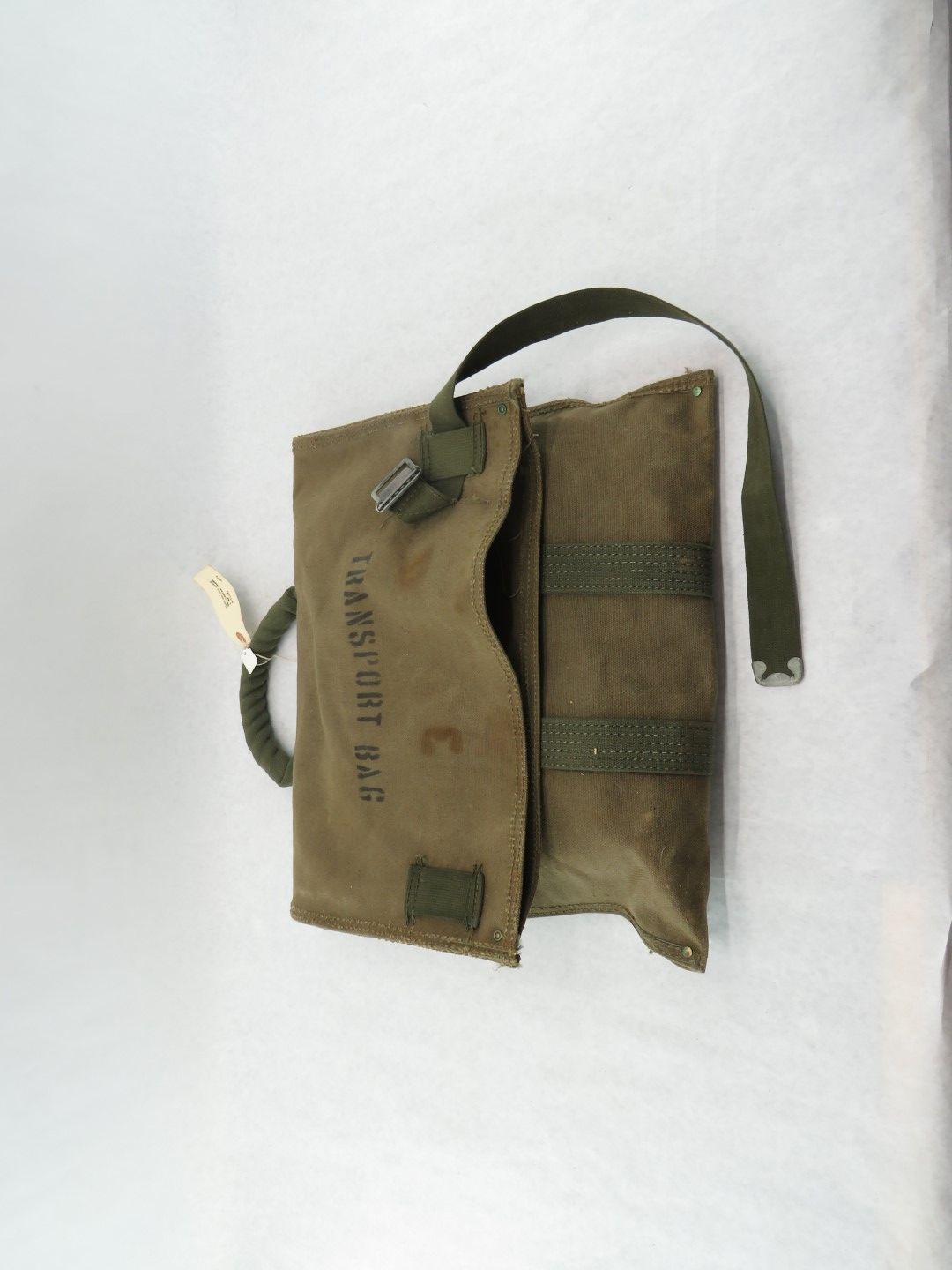Green canvas transport bag, open, with a strap and buckle, on a white surface.