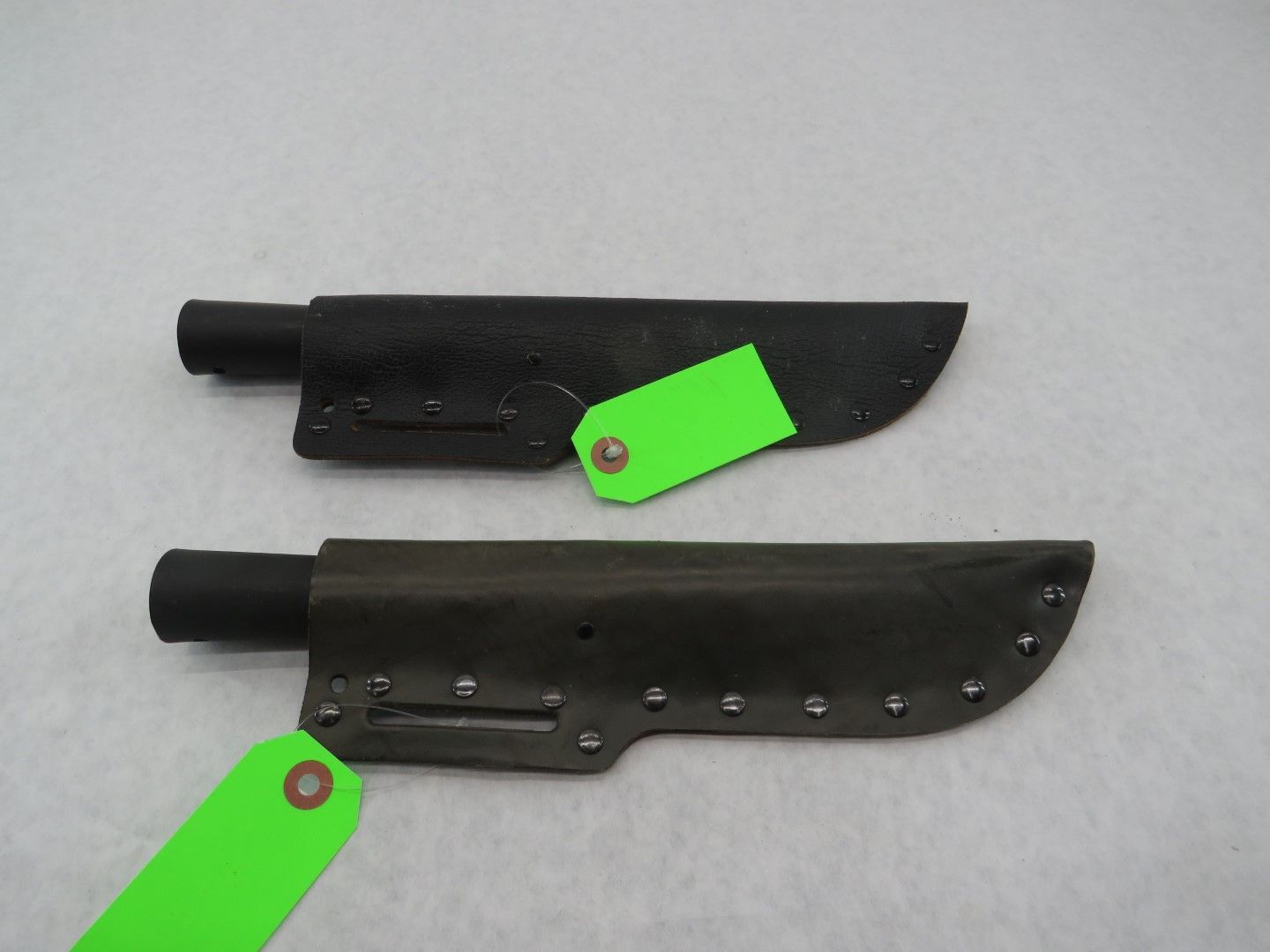 Two black leather knife sheaths with green tags.