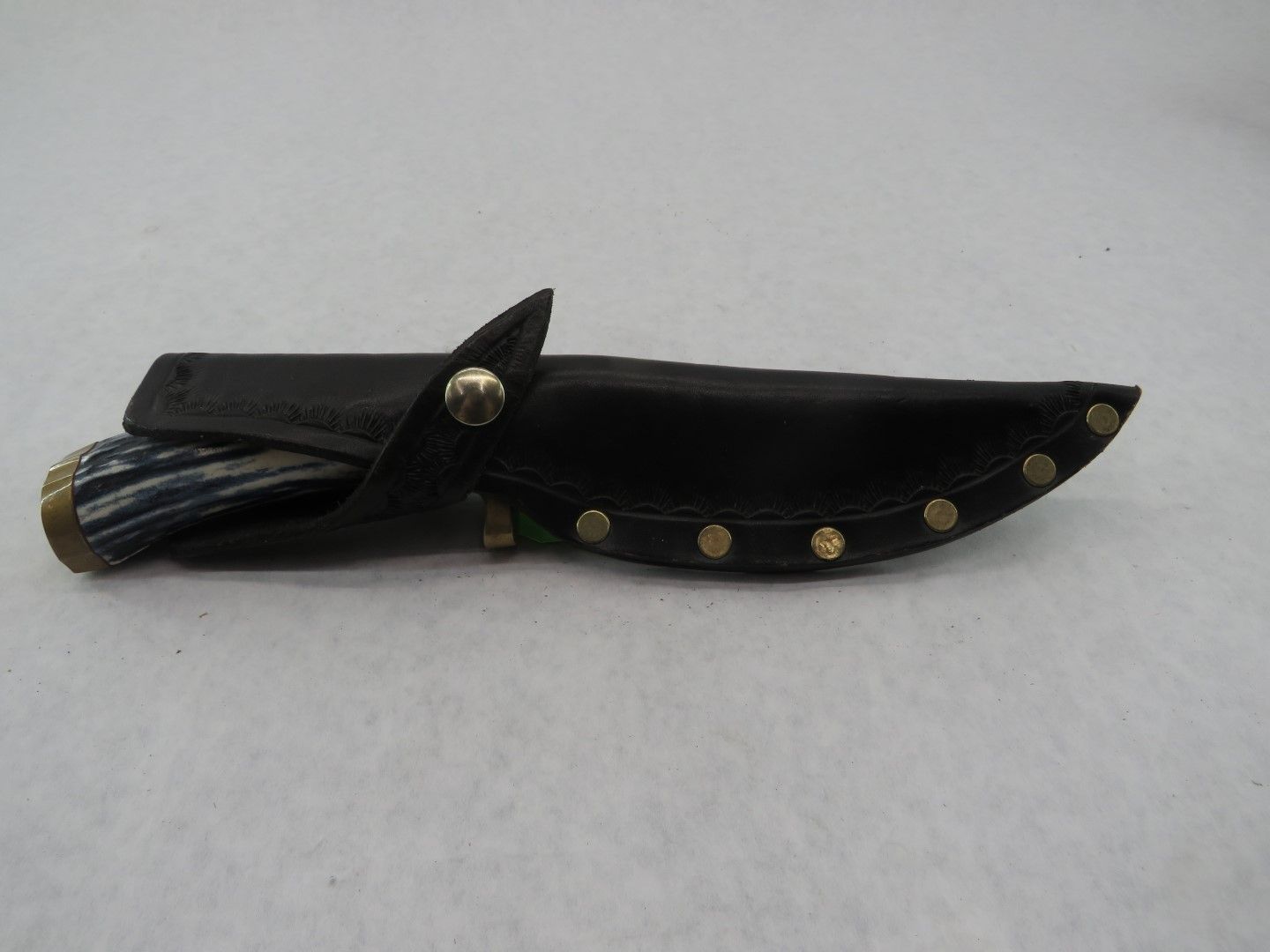 Knife with a black leather sheath; brass-colored rivets secure the sheath.
