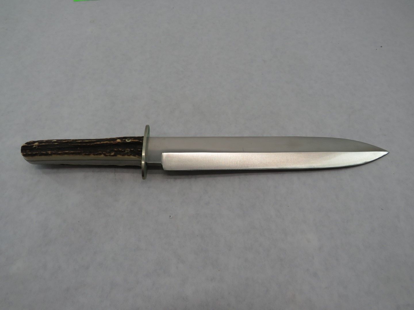 A hunting knife with a brown antler handle, a stainless steel blade, and a guard.