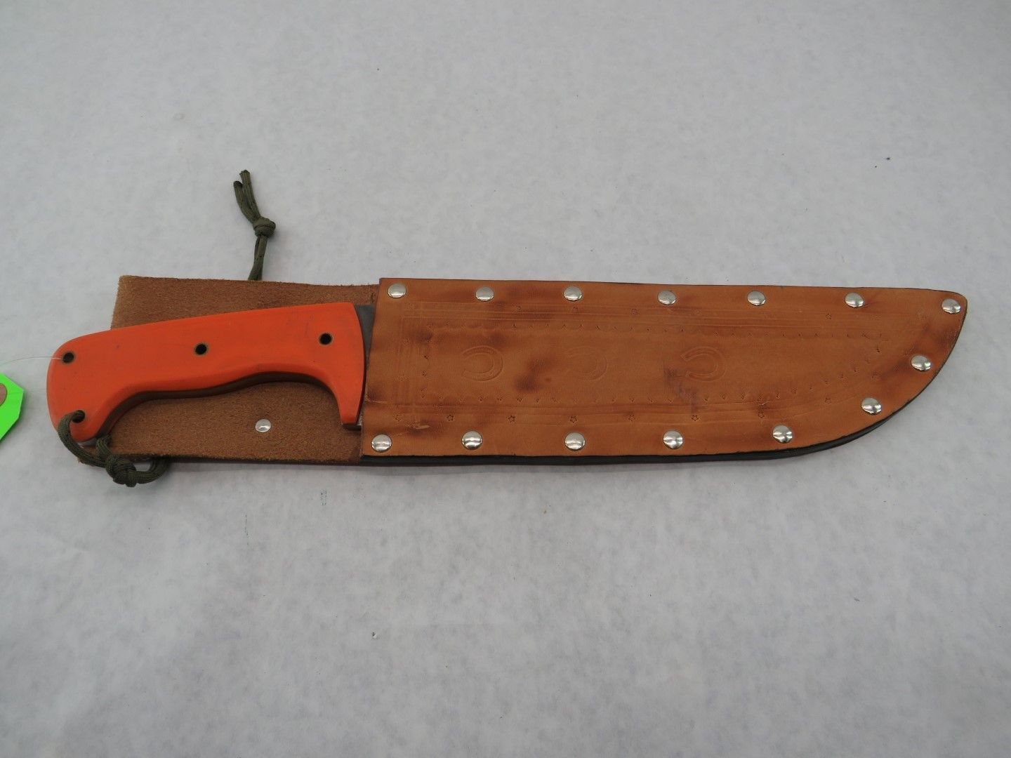 Orange-handled knife in a brown leather sheath with metal rivets.