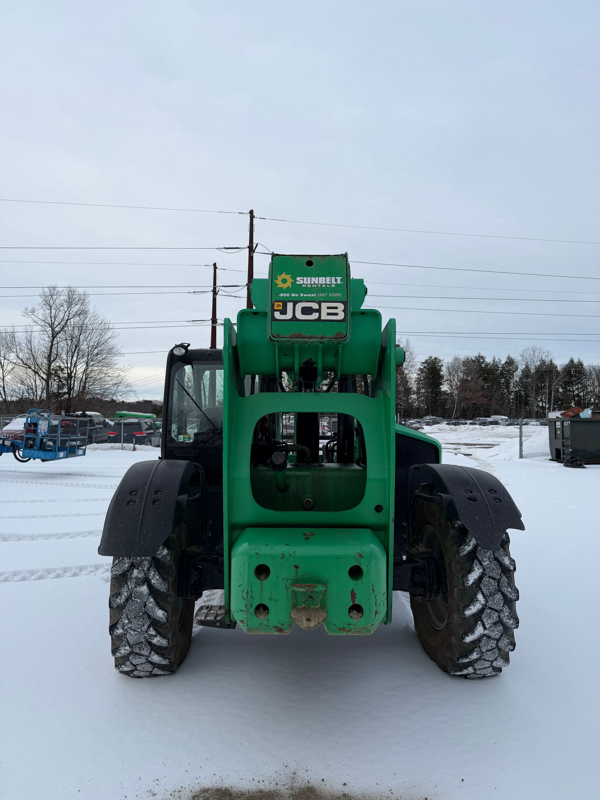 Green JCB telehandler on snowy ground, front view with large tires and overcast sky.