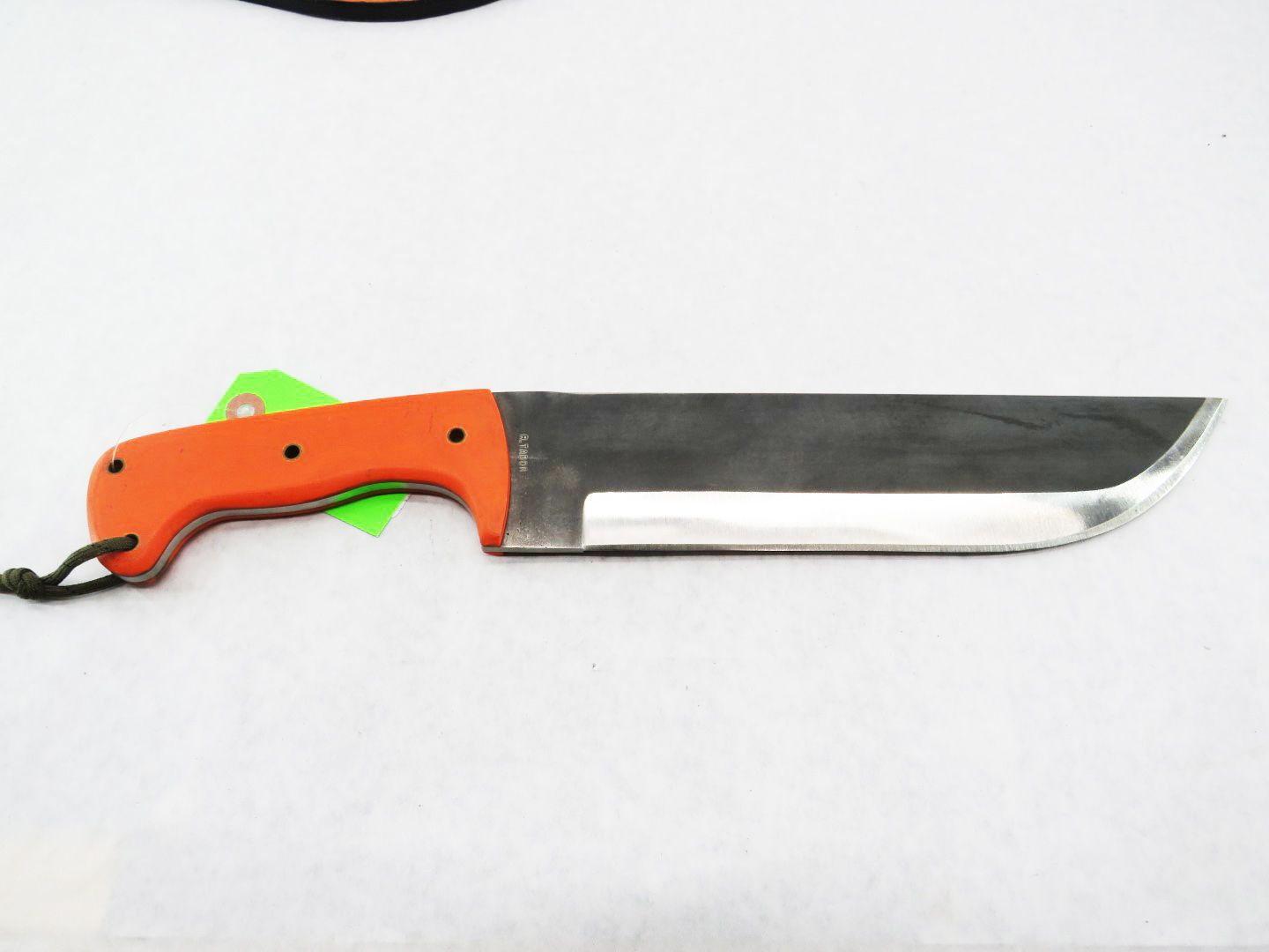 Large, orange-handled survival knife with dark blade, resting on a white surface. Green tag attached.