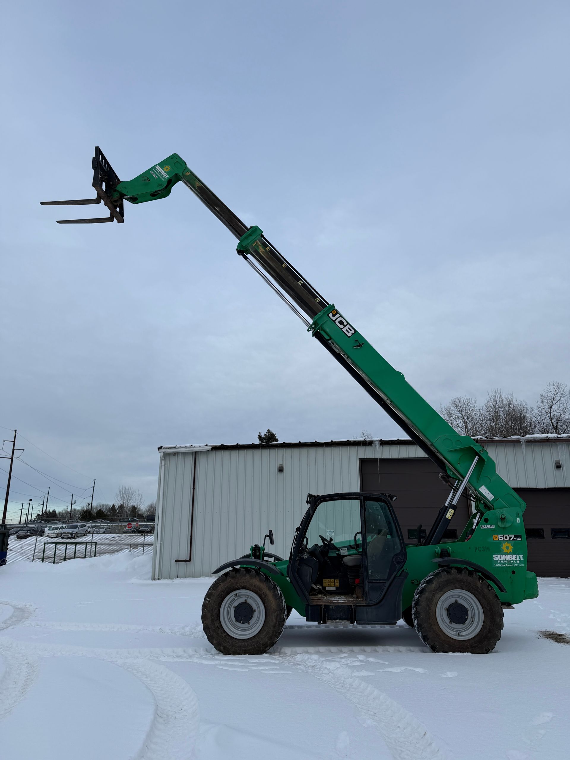 Green telehandler lifting a small load beside a snowy building outdoors