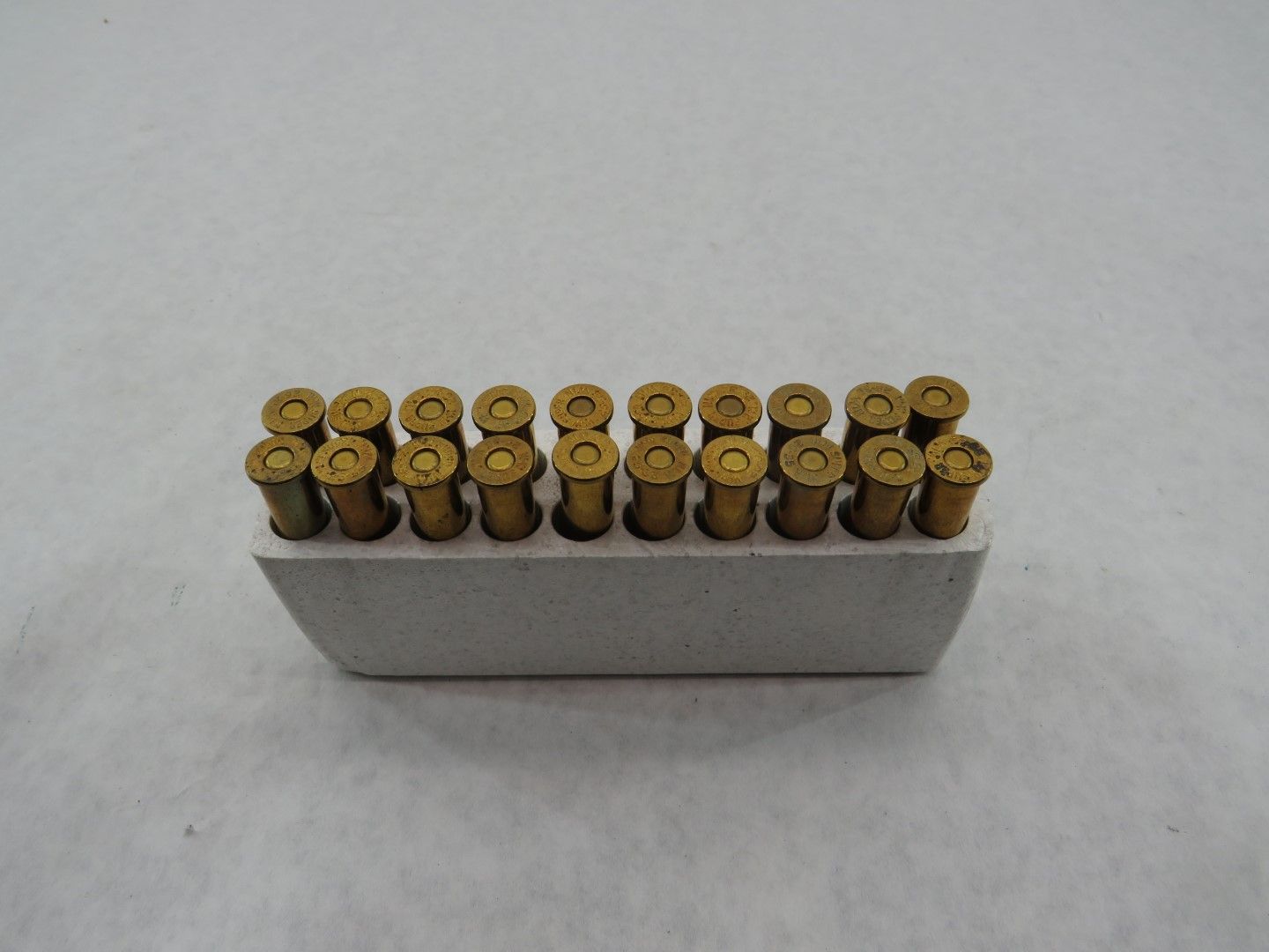 A tray of twenty-four brass-colored bullets in a white, rectangular holder.