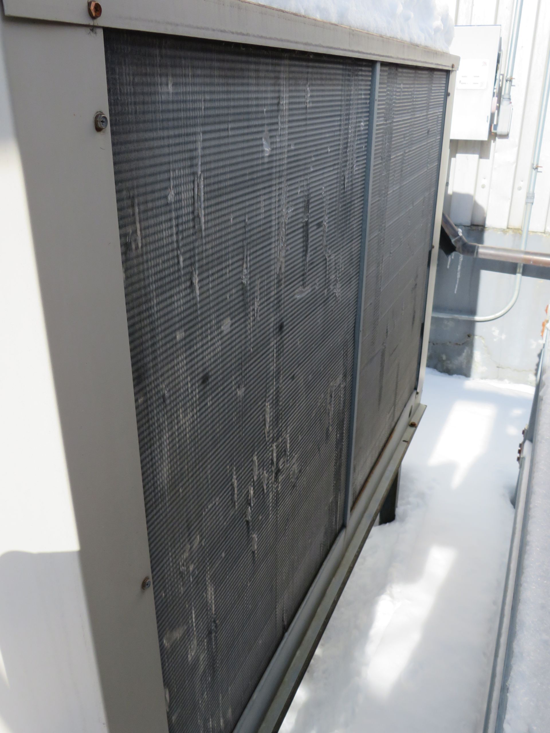 Outdoor air conditioning unit with iced-over coils on a snowy rooftop.