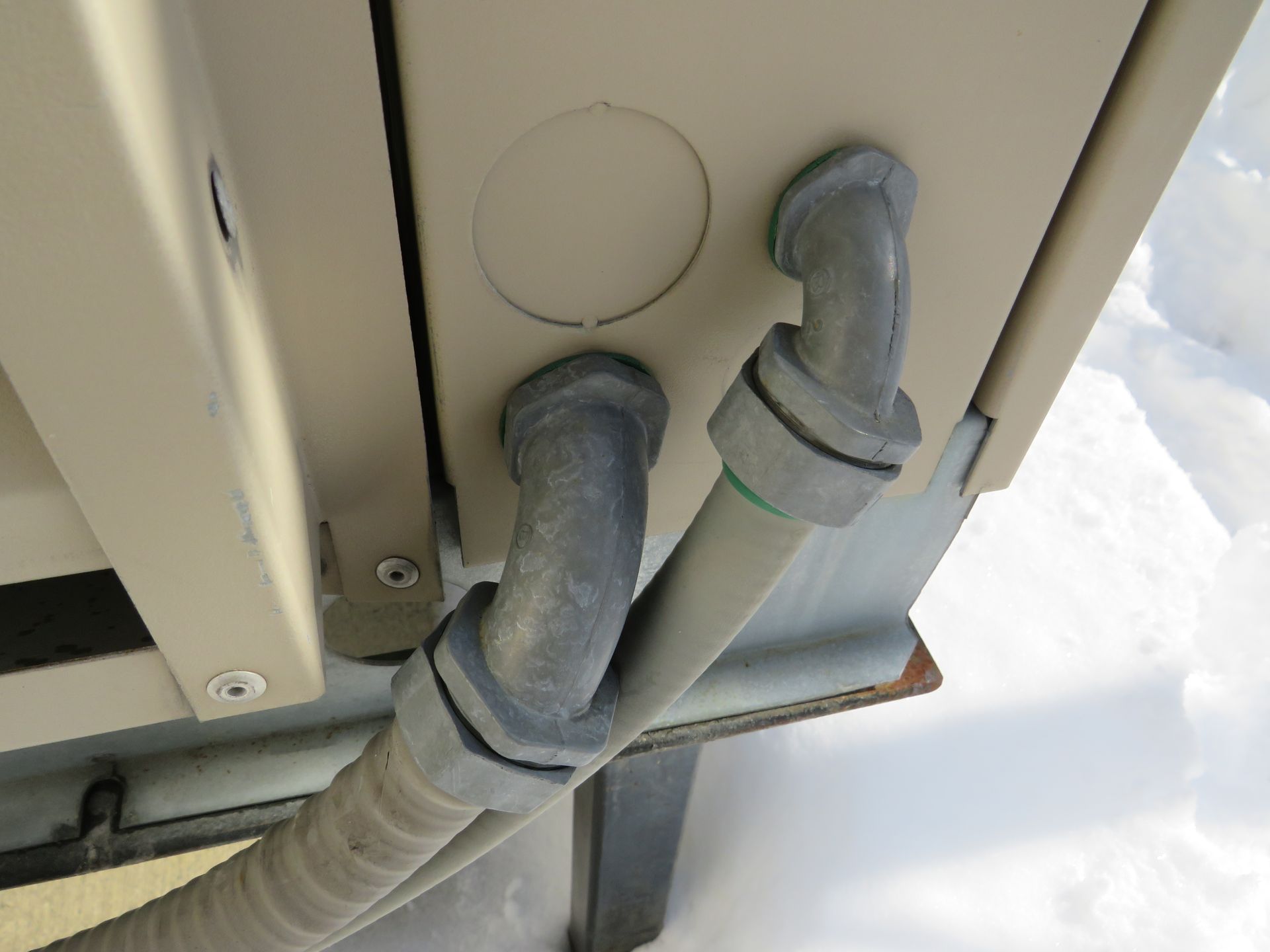 Close-up of gray conduit pipes entering a beige electrical box. Snow visible in the background.