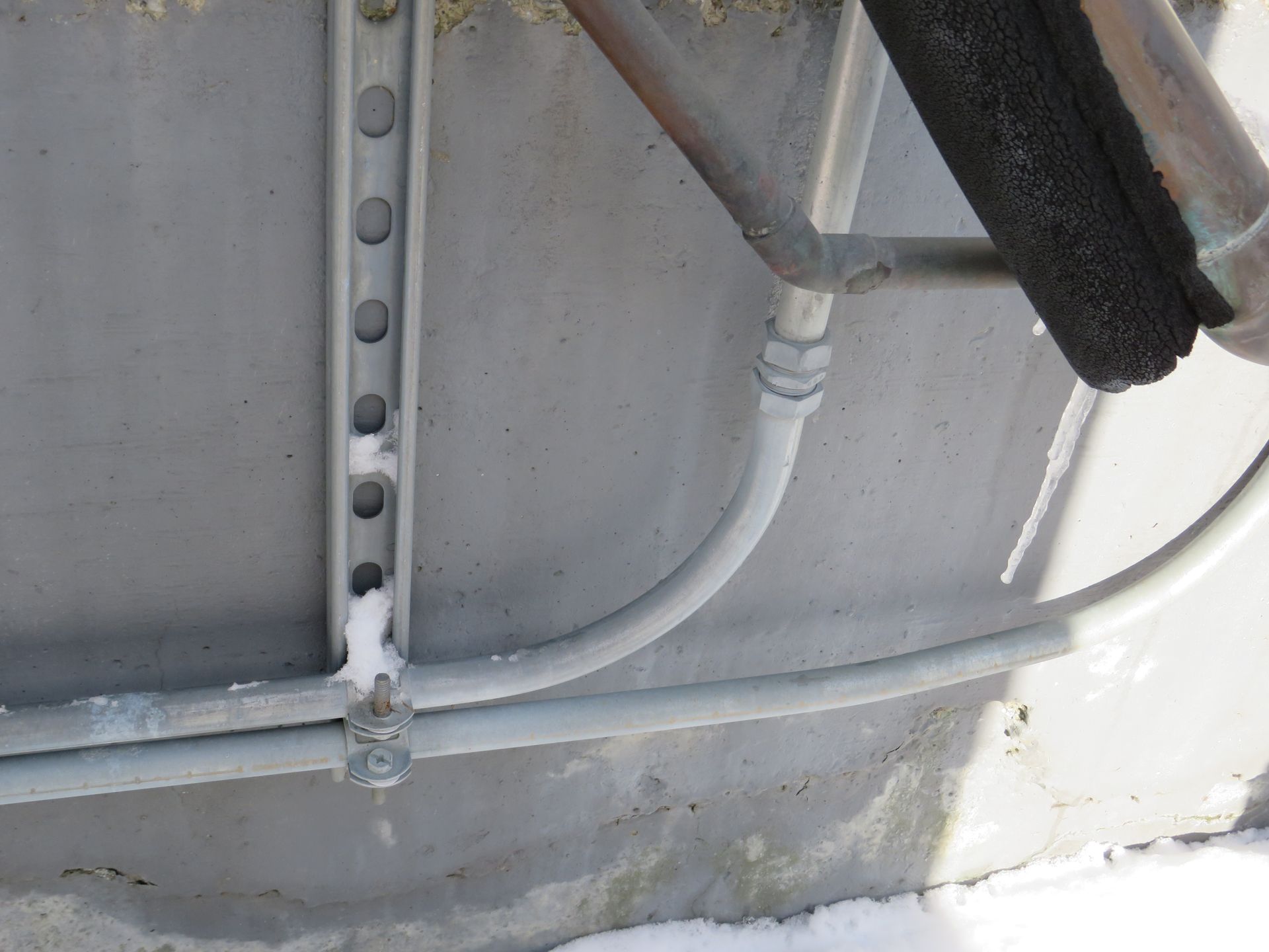 Gray pipes and conduit on a concrete wall.