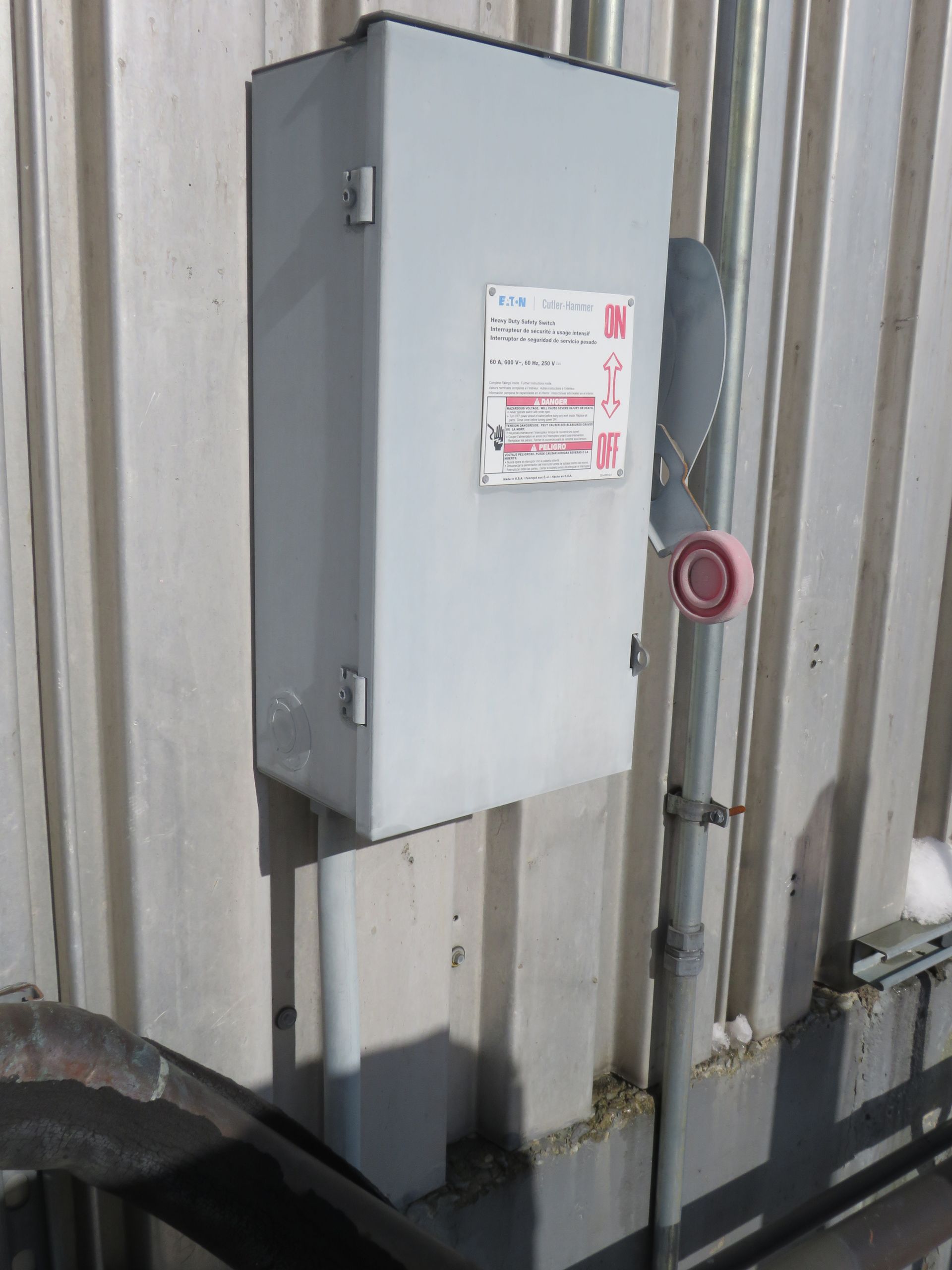 Gray electrical box mounted on a corrugated metal wall, with a red emergency shutoff button nearby.