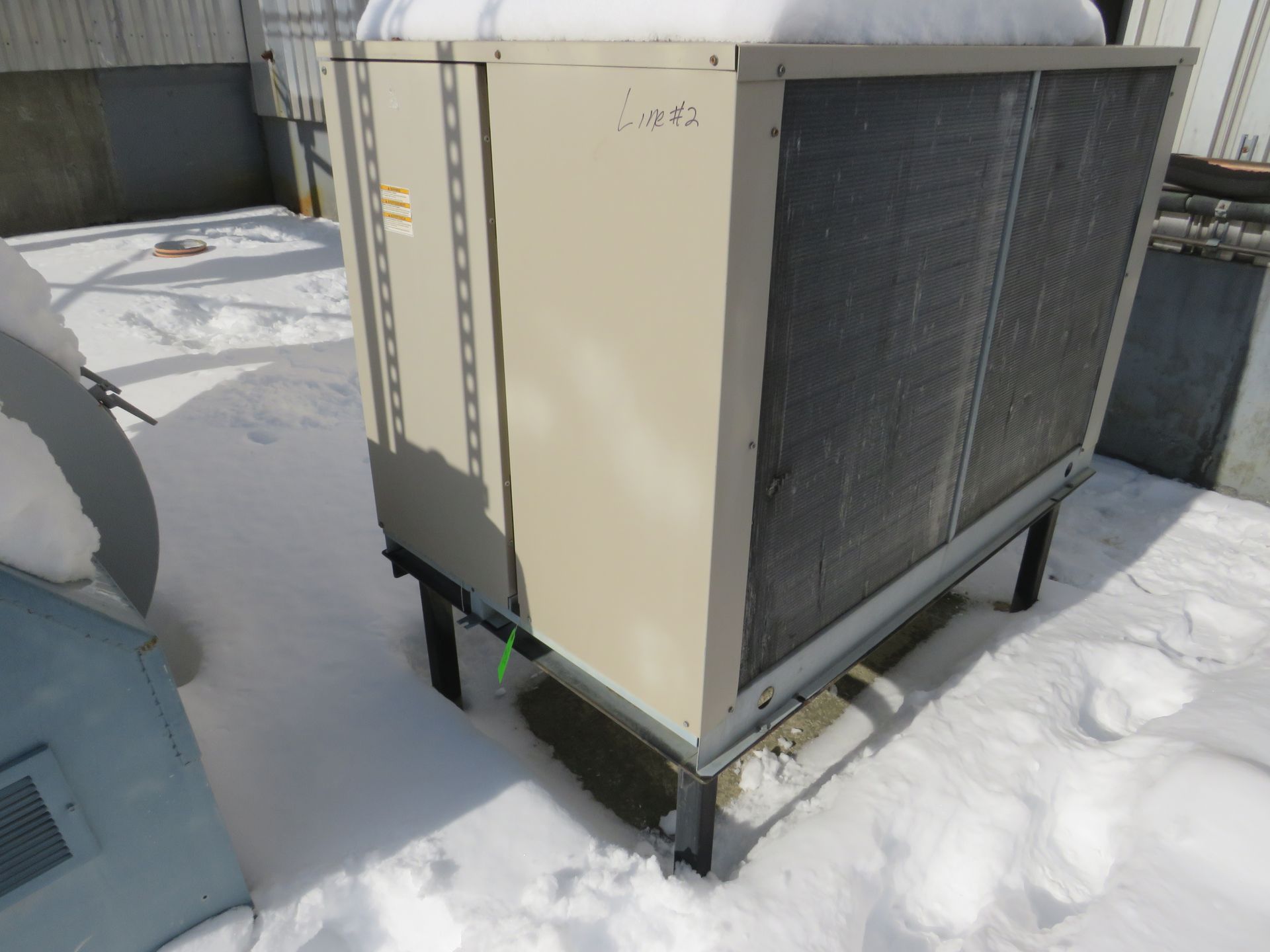 HVAC unit on a snow-covered rooftop. Gray metal and a black base, with a screened side.