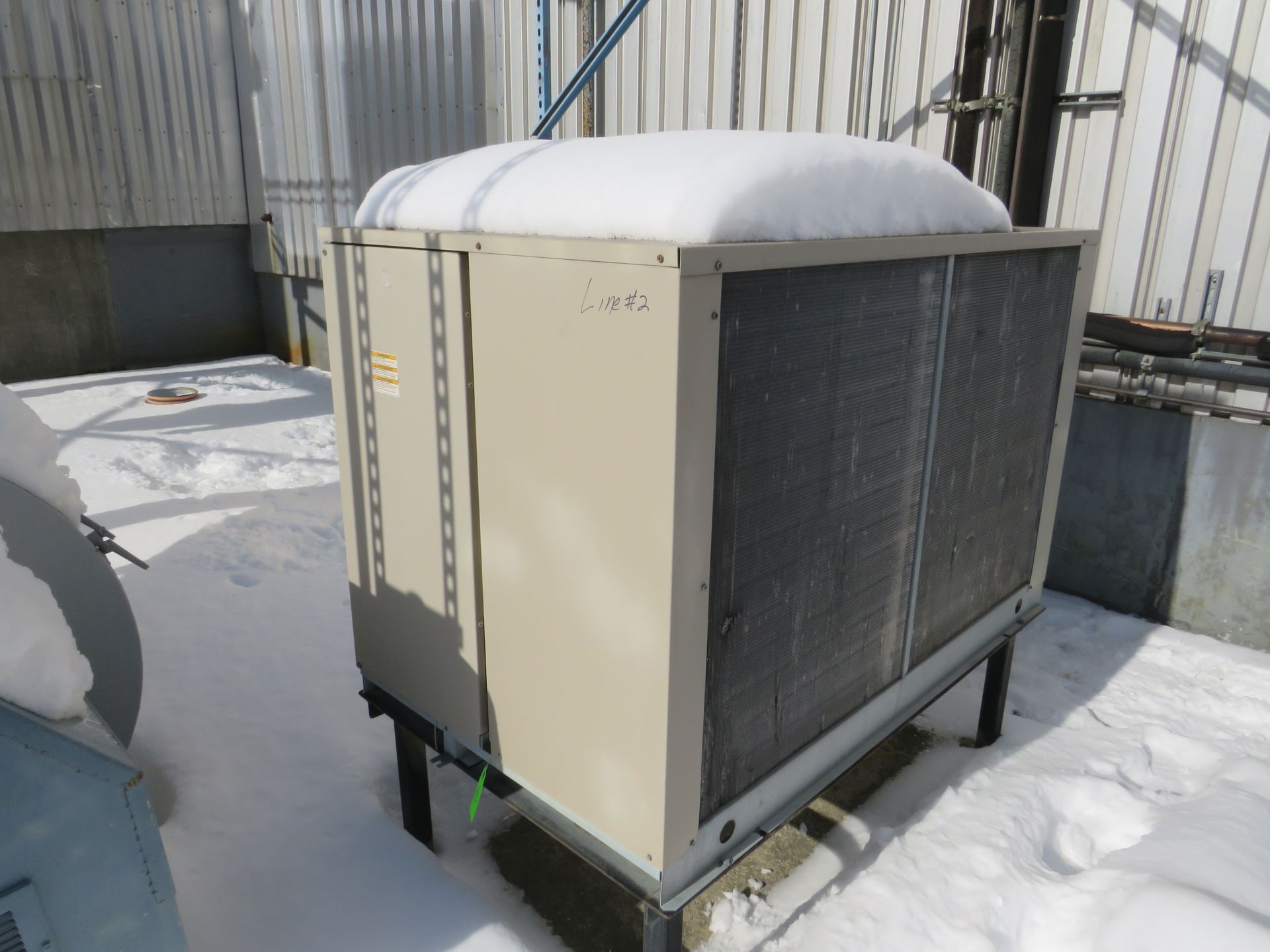 Outdoor air conditioning unit covered in snow, beige and metal with a mesh front.