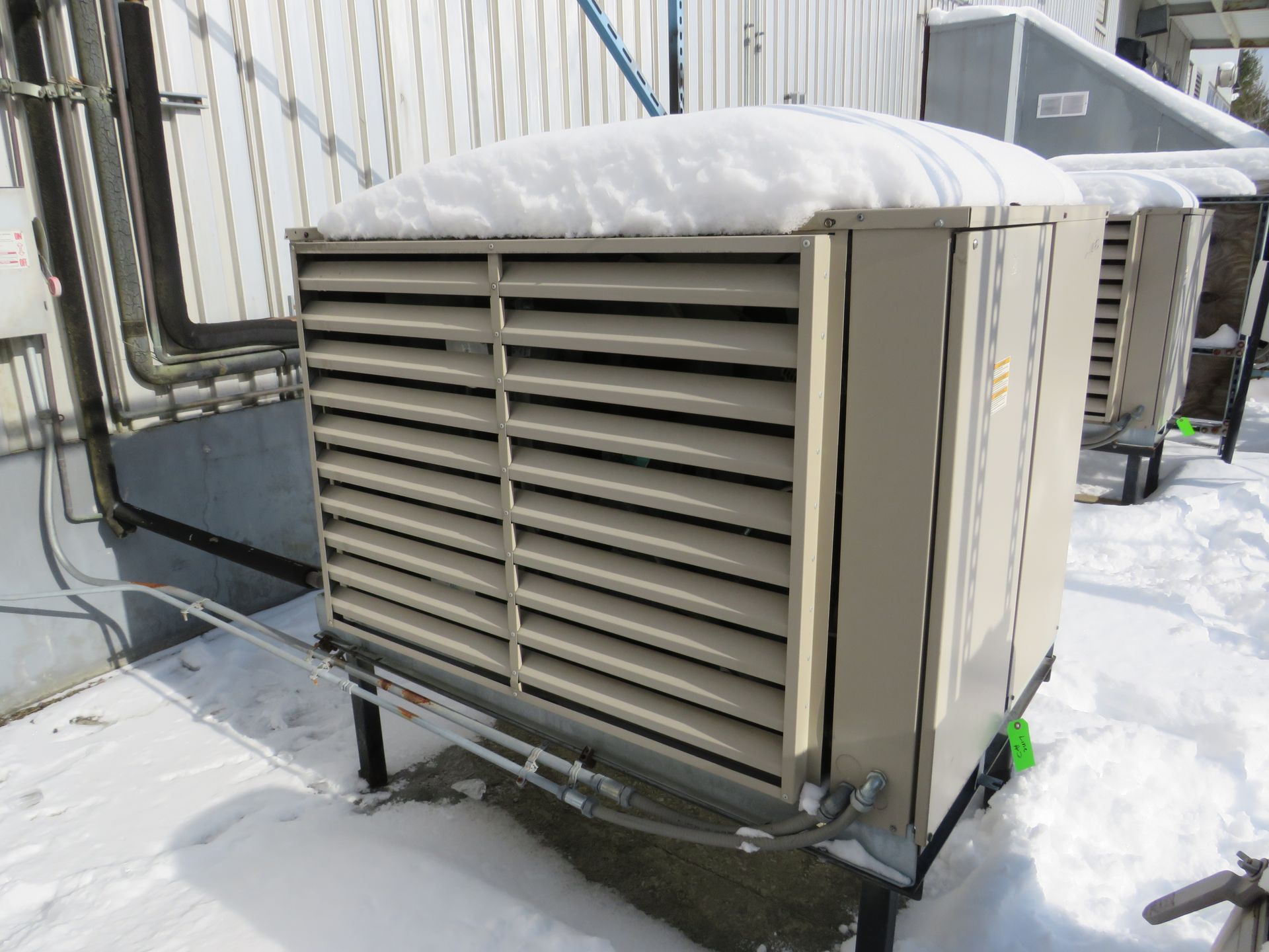 A beige industrial cooling unit covered in snow stands outdoors in a snowy environment.
