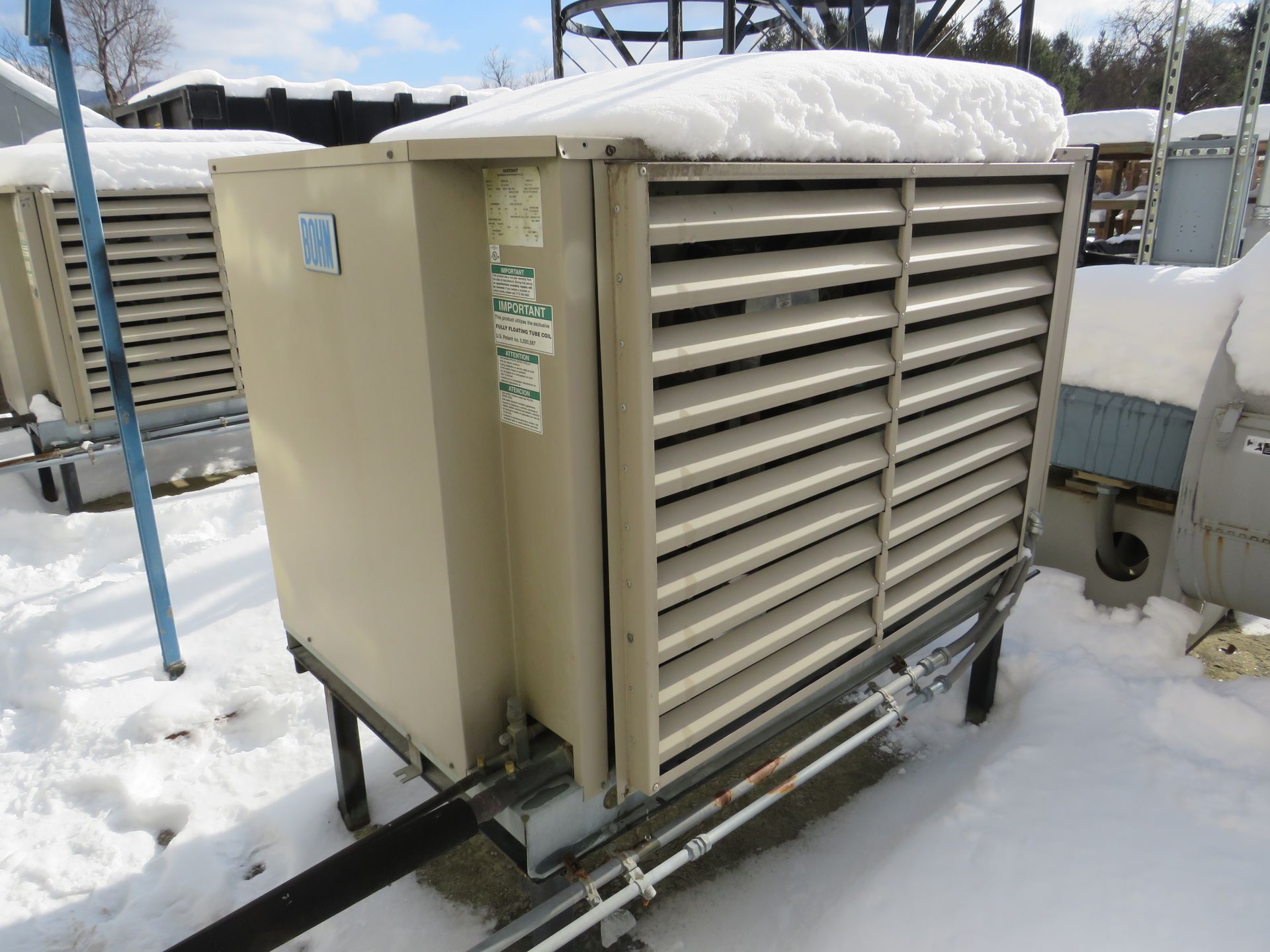 Large beige industrial cooler unit with snow on top, outdoors.
