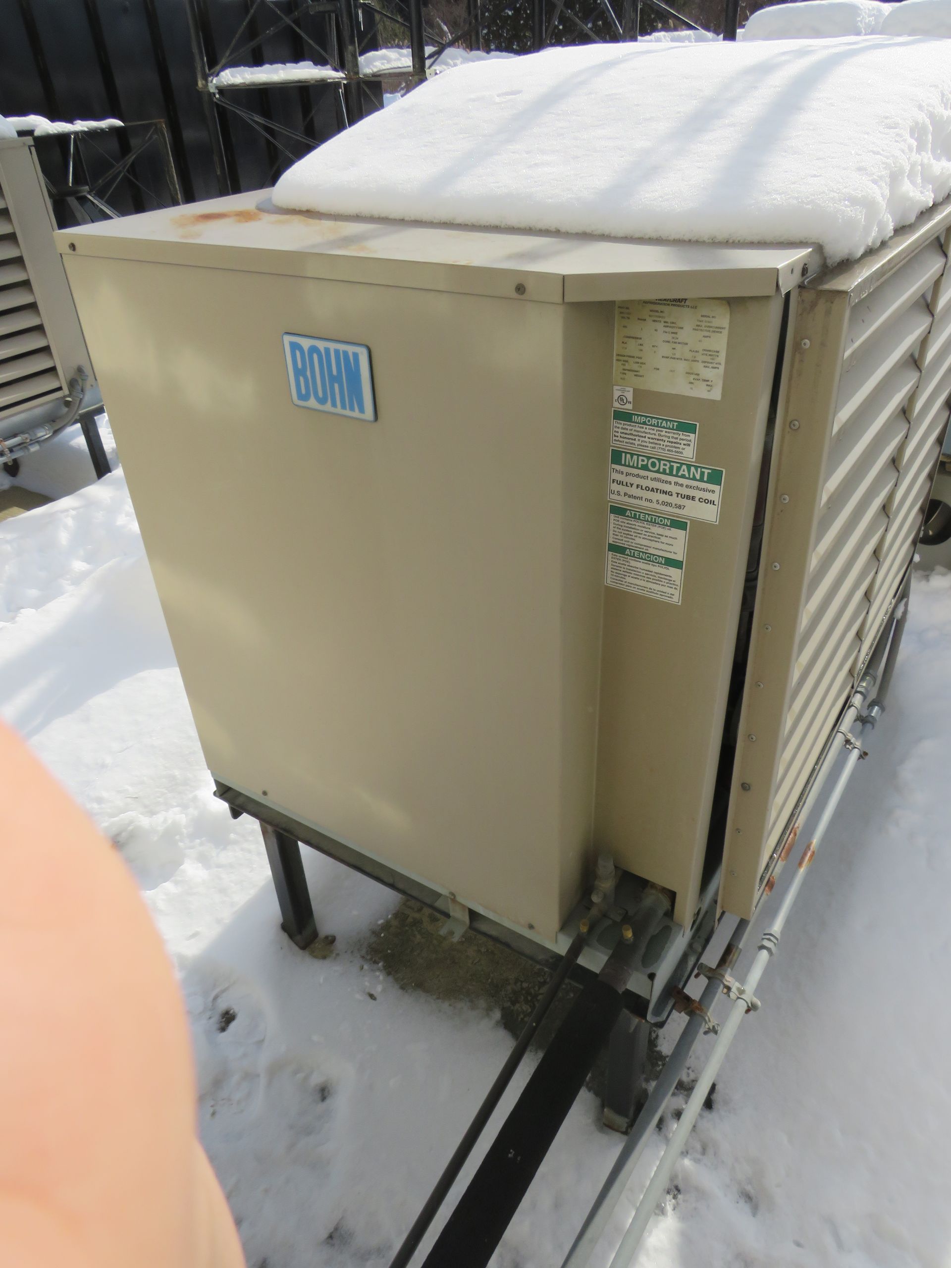 An industrial beige cooling unit covered in snow on a snowy day.