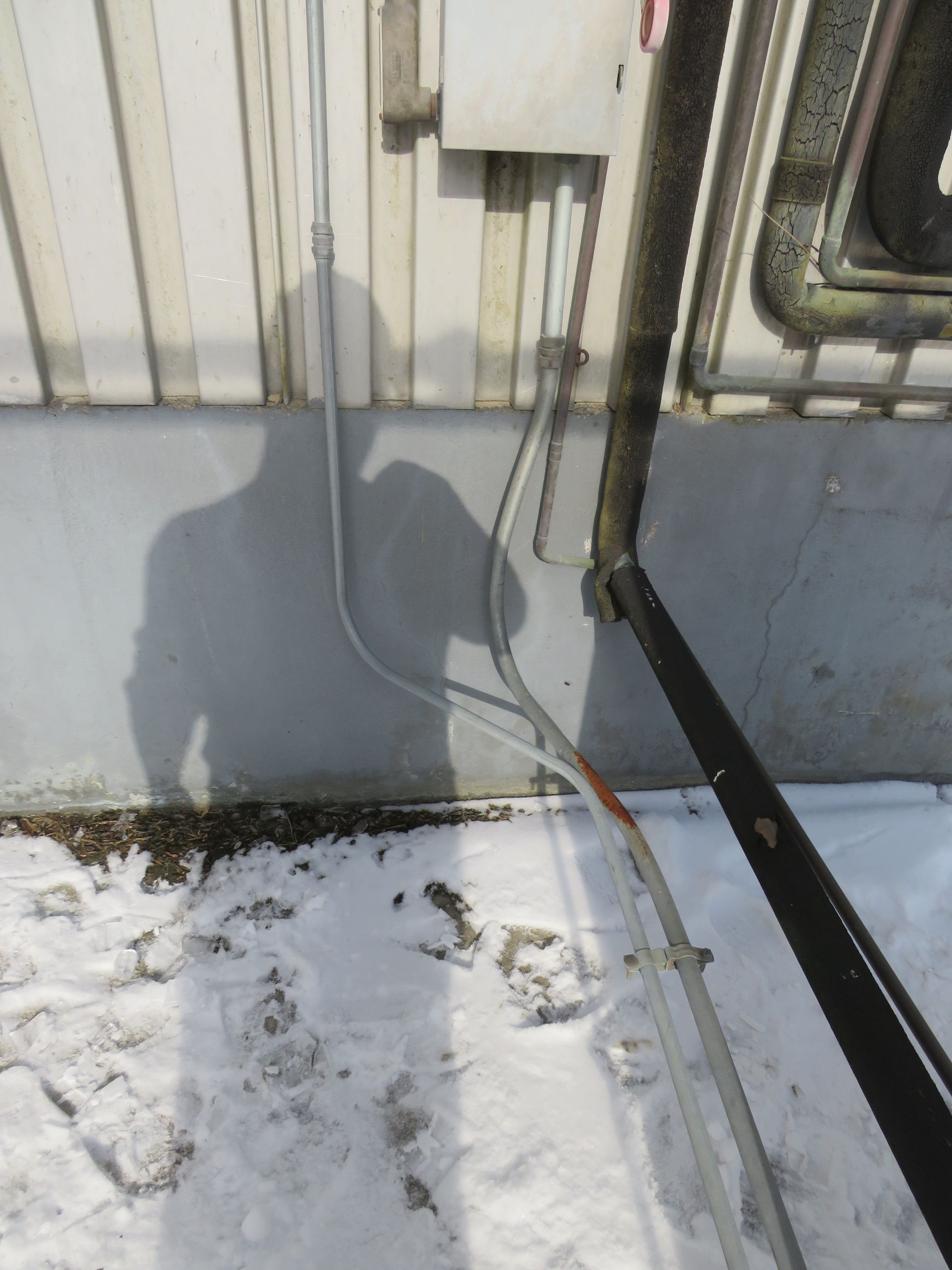 Electrical conduit and a black pole in a snowy outdoor setting.