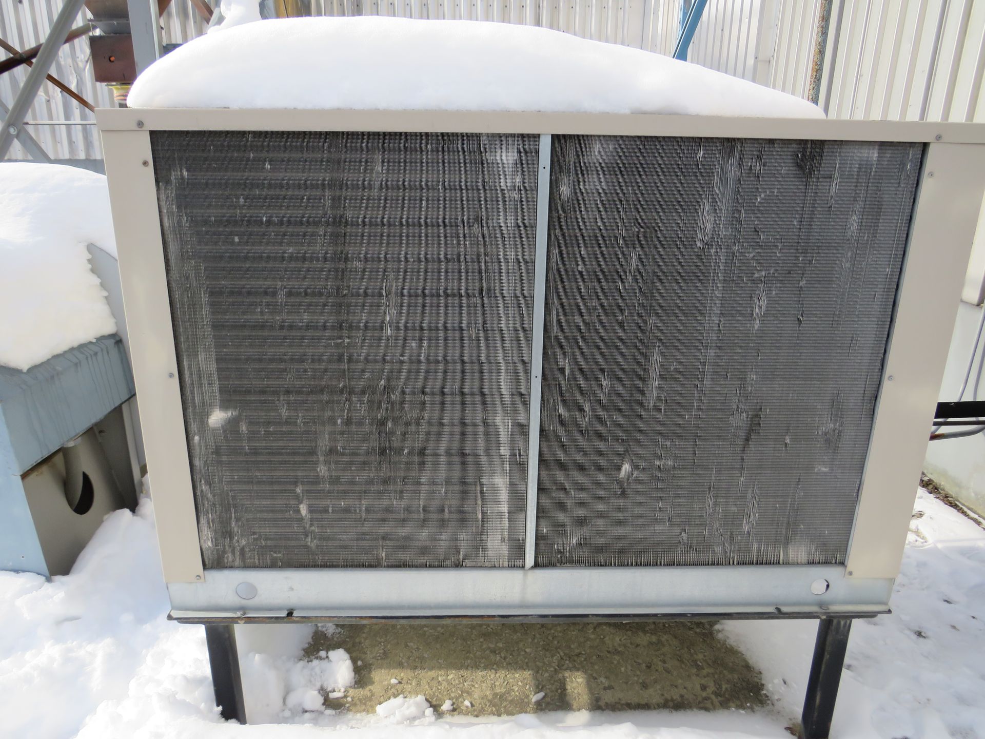 An outdoor air conditioning unit covered in snow on a snowy day.