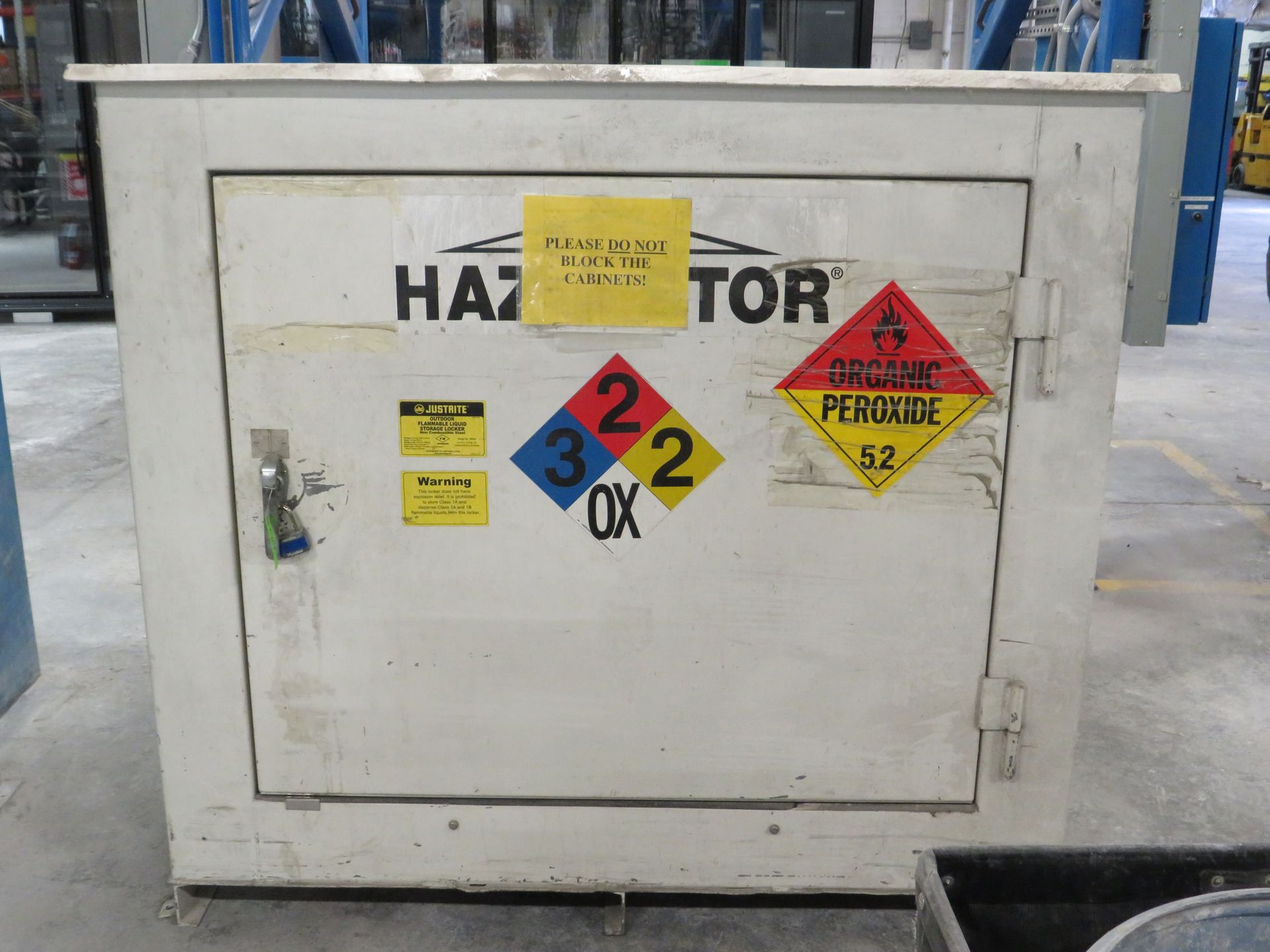 White cabinet with hazard warning labels: flammable, oxidizer, and organic peroxide, in a warehouse setting.