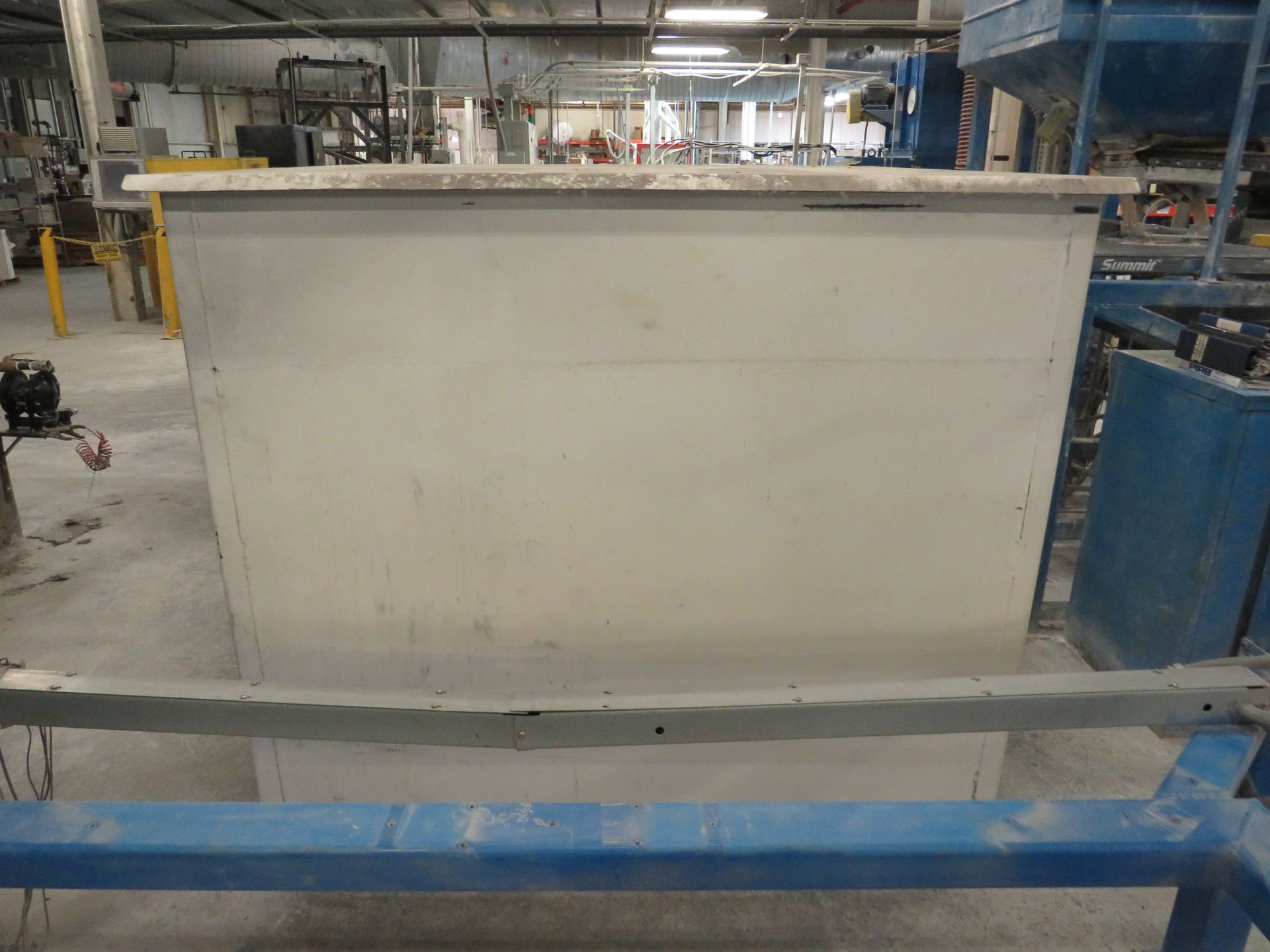 A large, pale-colored rectangular industrial container in a factory setting, with metal and machinery visible.
