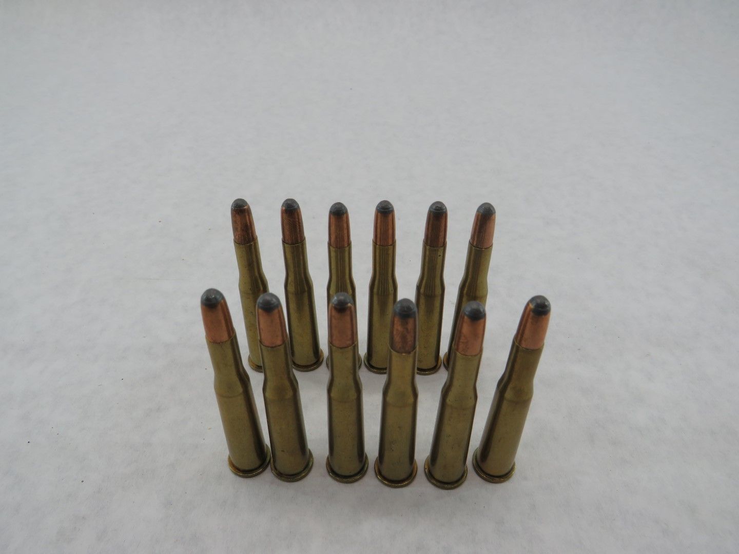 Ten rifle cartridges standing upright on a white surface.